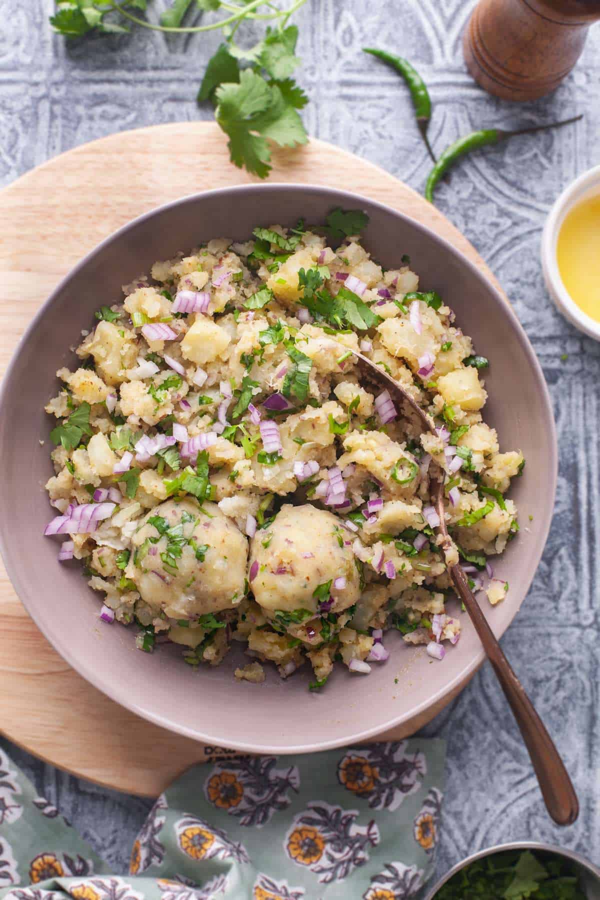 Aloo Bharta in a bowl garnished with chopped onions and cilantro on a printed grey background.
