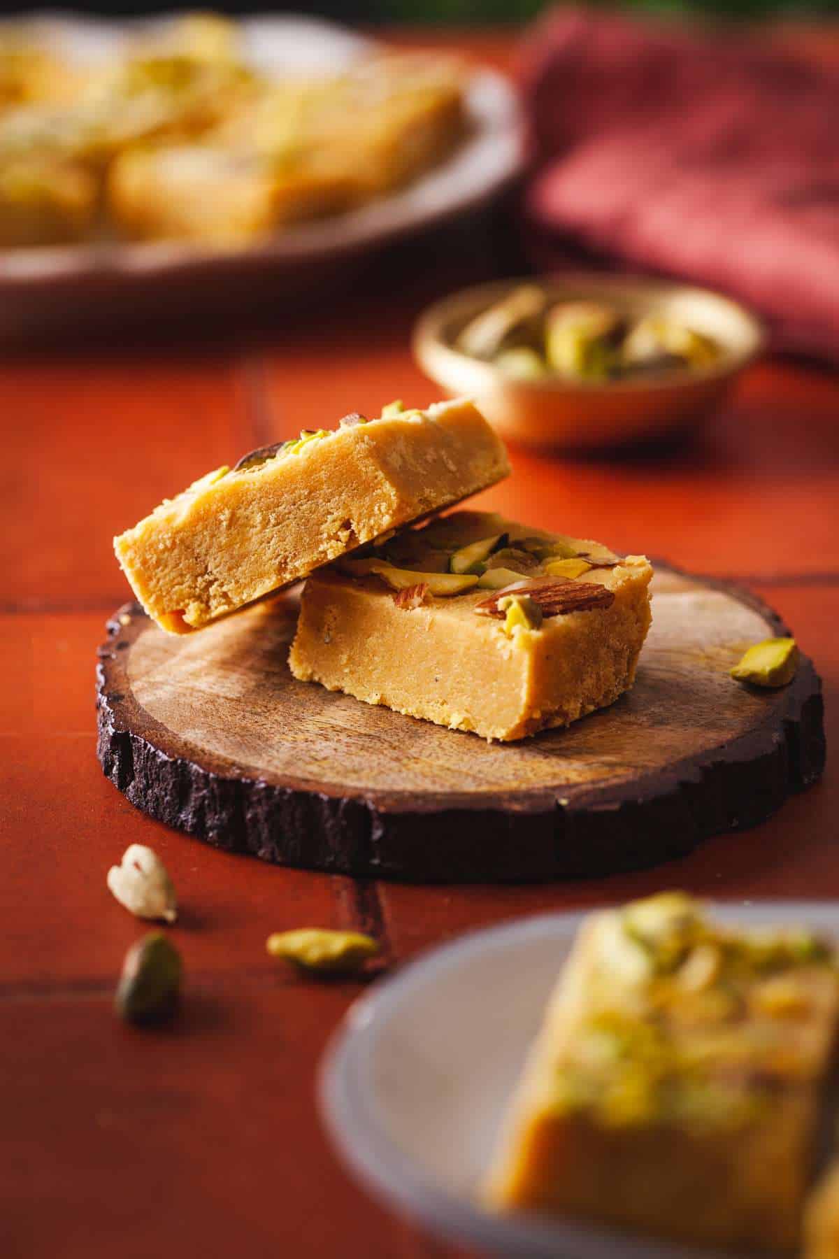 Two pieces of besan barfi placed on a small wood piece.