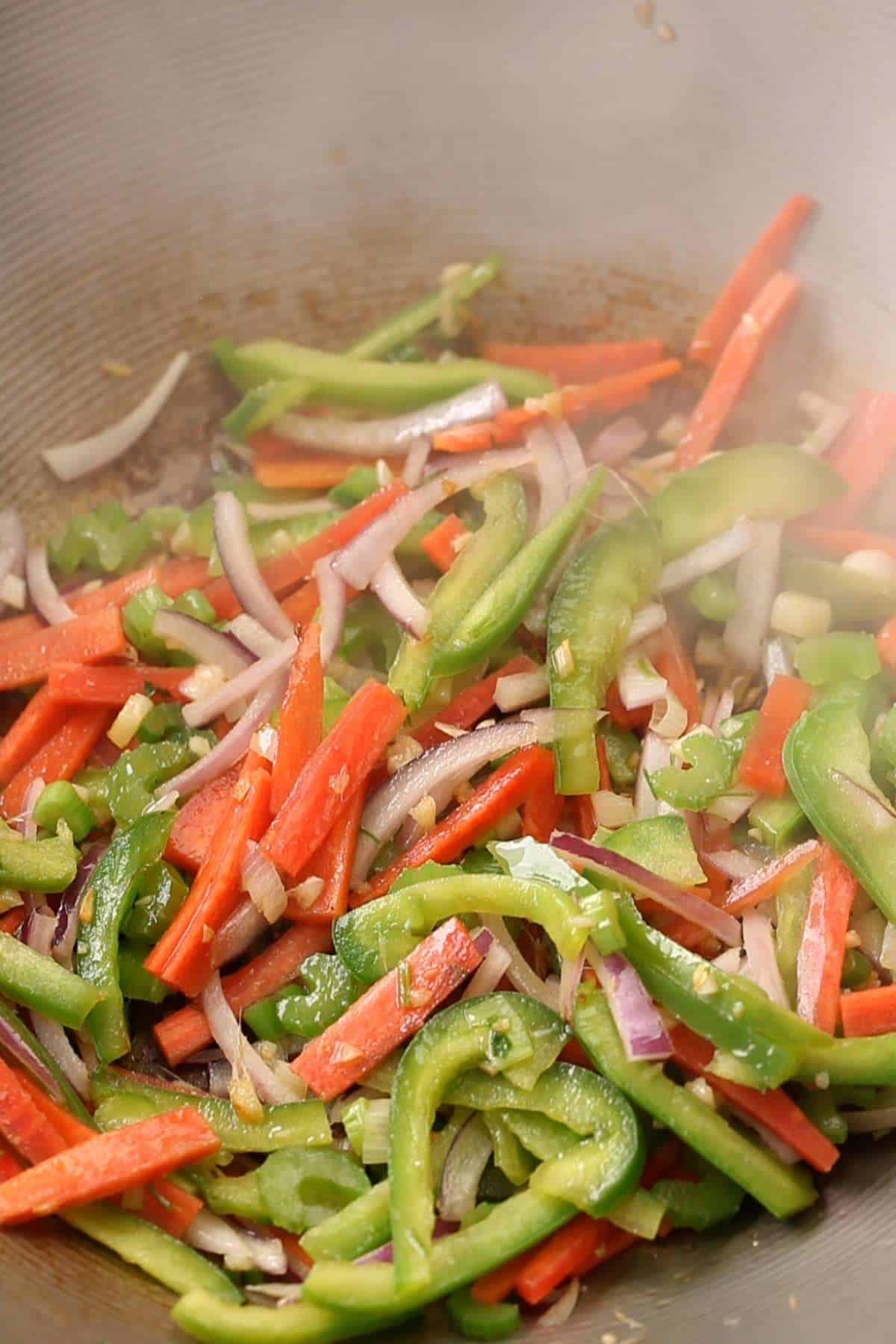 Vegetables stir frying on high heat in a wok. 