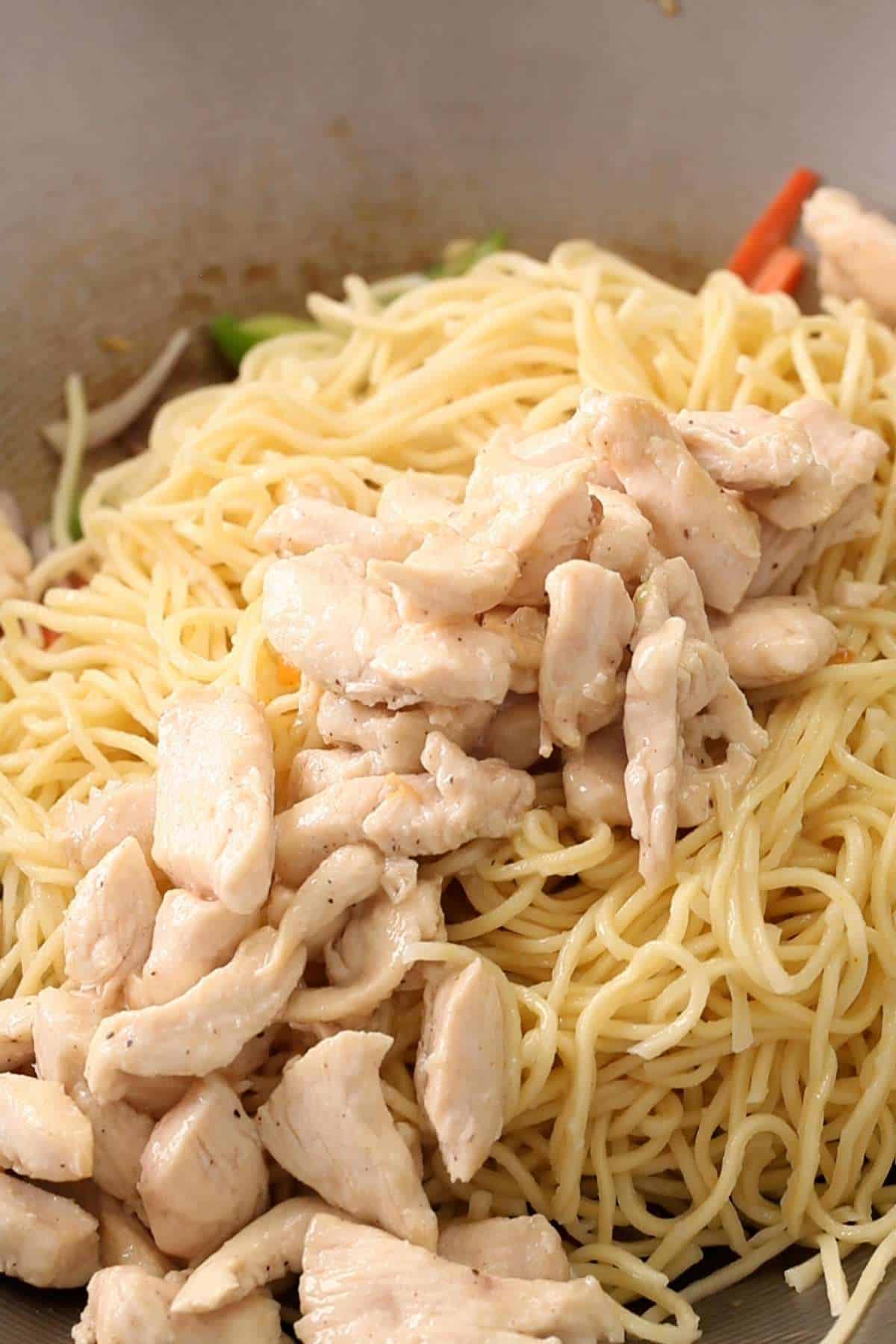 Adding boiled noodles and cooked chicken on top of vegetables. 