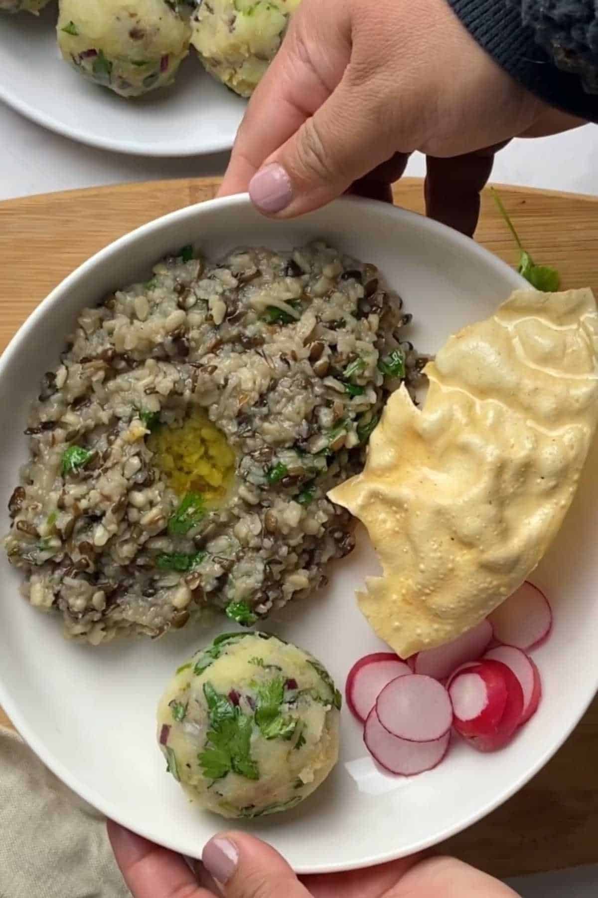 Warm urad dal khichdi served with sides like aloo bharta, radish and papad.