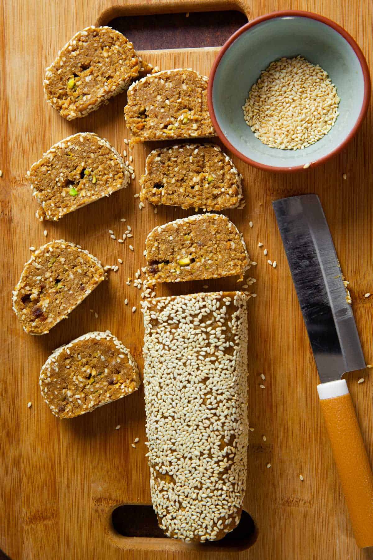 A roll of cut up mawa and til and a bowl of white sesame seeds.