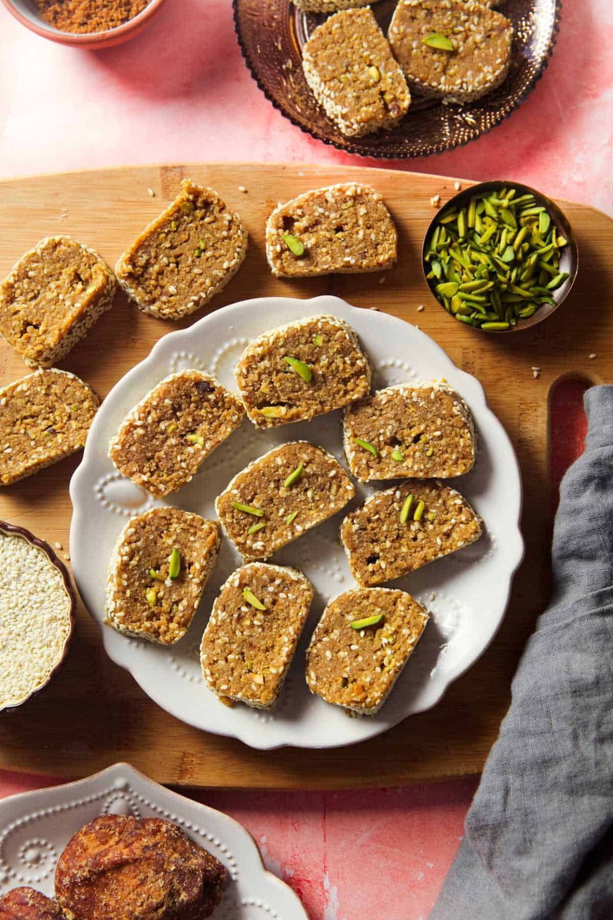 Mawa Til Roll in a white plate with a bowl of pistachios.