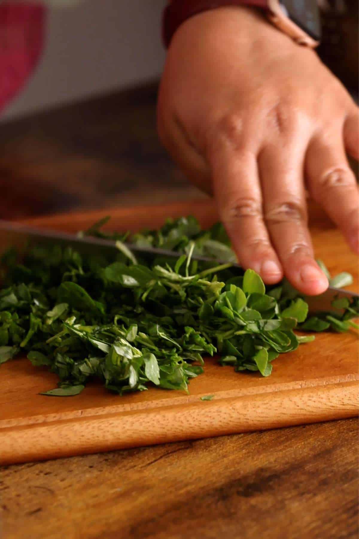 Chopping fresh methi leaves on a wooden board.