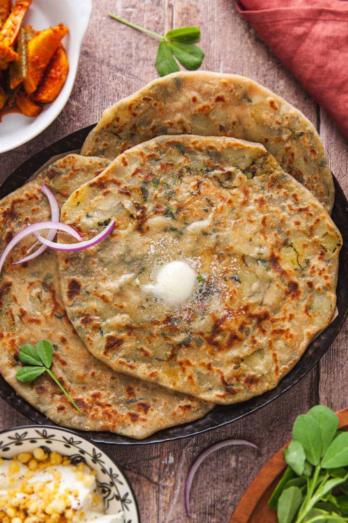Close up view of methi aloo flatbreads with butter melting on top. 