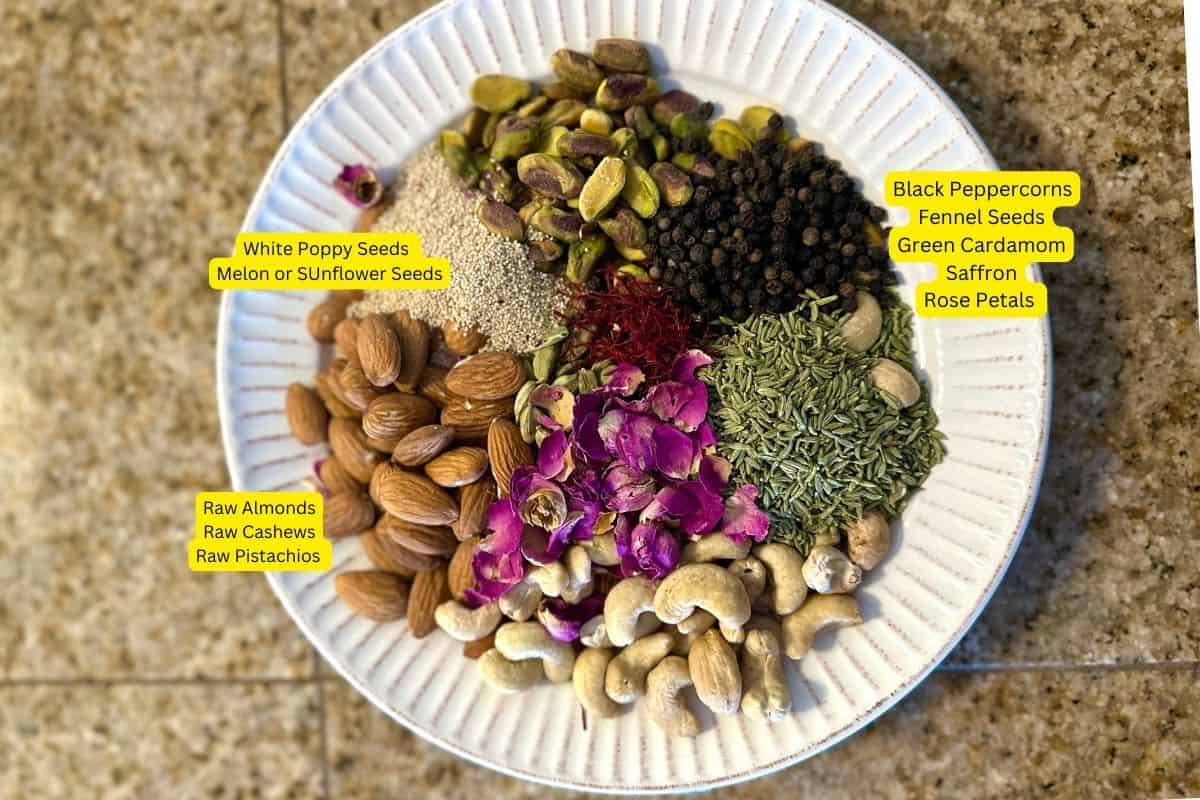 Spices. nuts and seeds needed for making thandai masala powder placed on a white plate. 