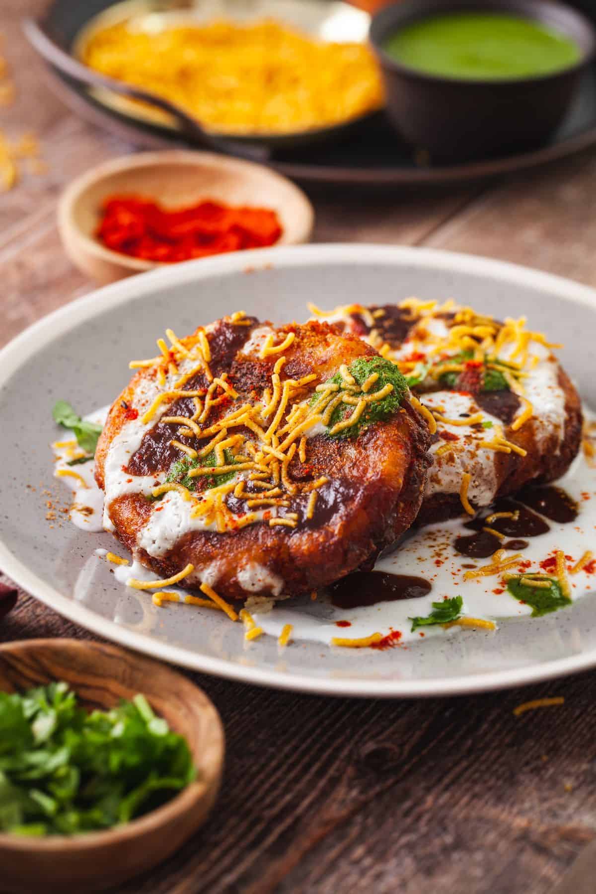 Aloo Tikki Chaat served on a grey colored plate with chaat toppings.