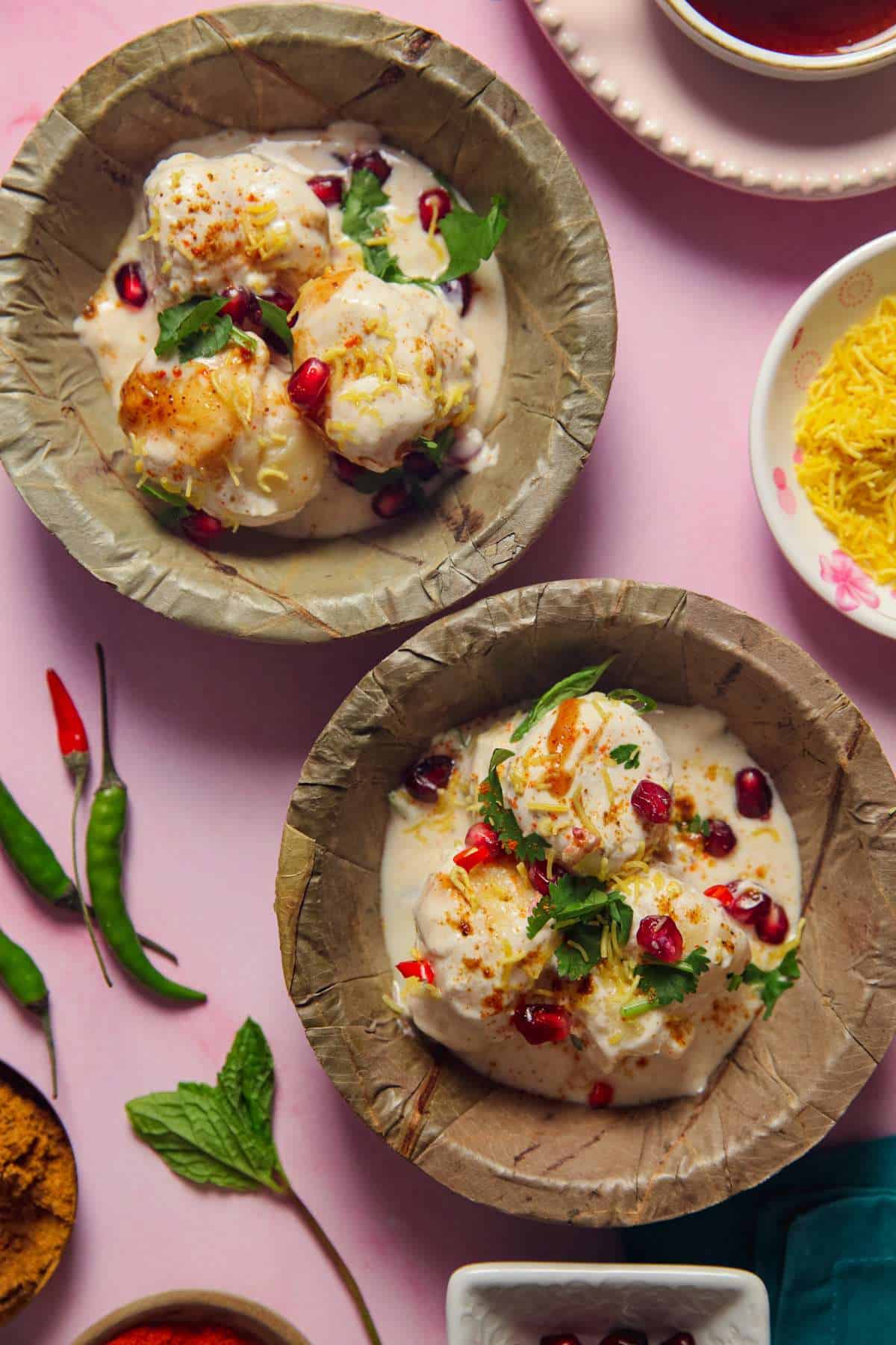 Moong Dal Dahi Vada in a palm leaf bowls topped with chaat condiments, herbs and pomegranate seeds.