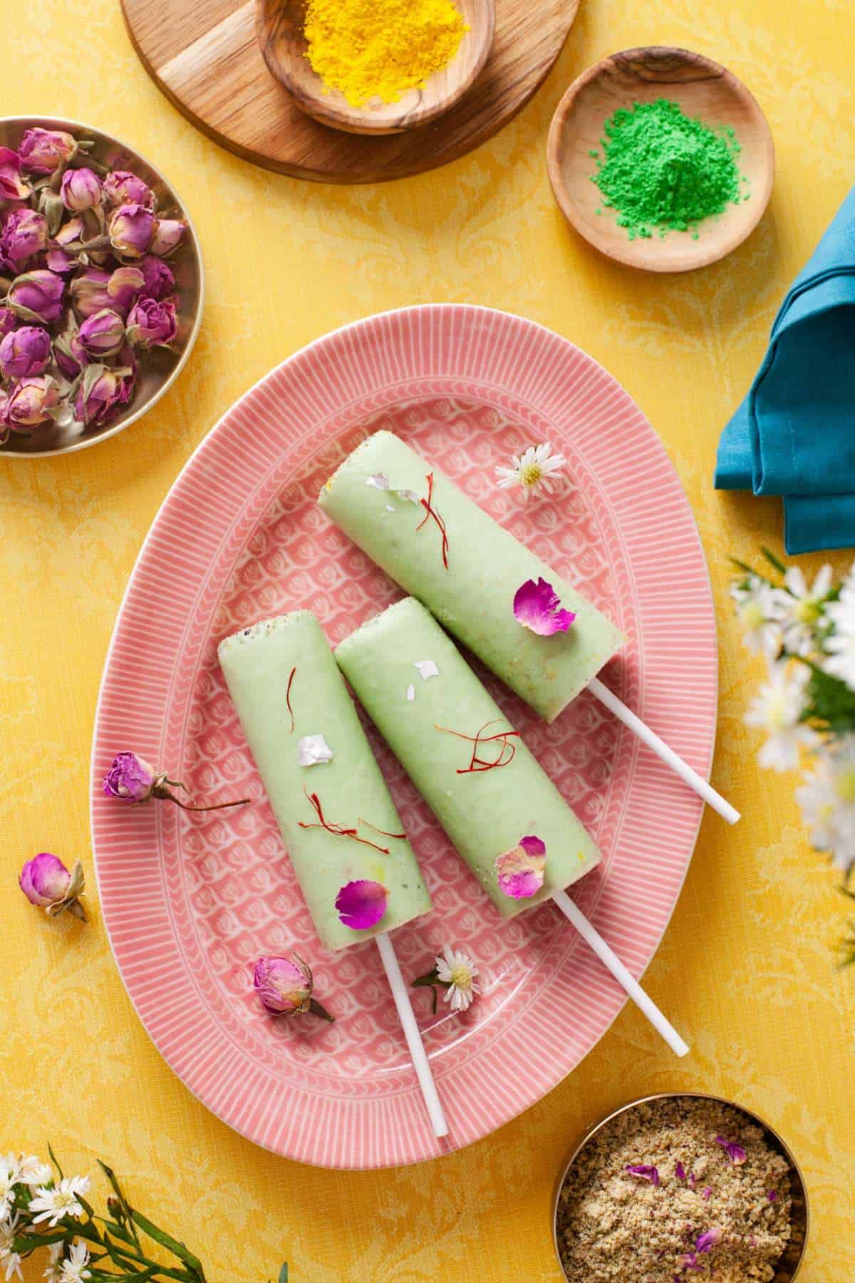 Paan Kulfi placed on a oval pink plate and garnished with edible silver foil, rose petals and saffron. 