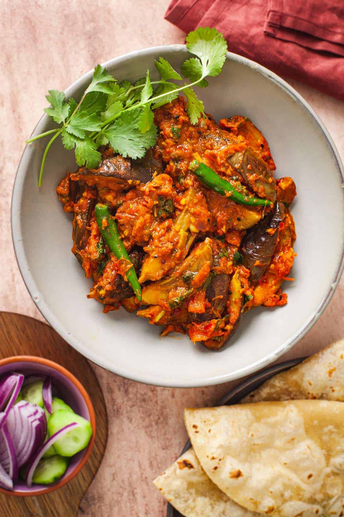 Achari Baingan in a grey bowl with a salad and flatbreads.