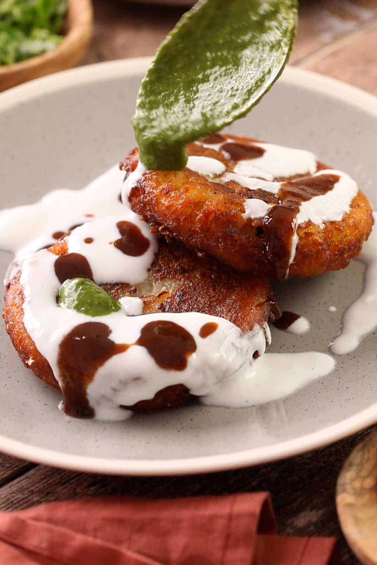 Topping aloo tikki with yogurt, green chutney and sweet tamarind chutney.