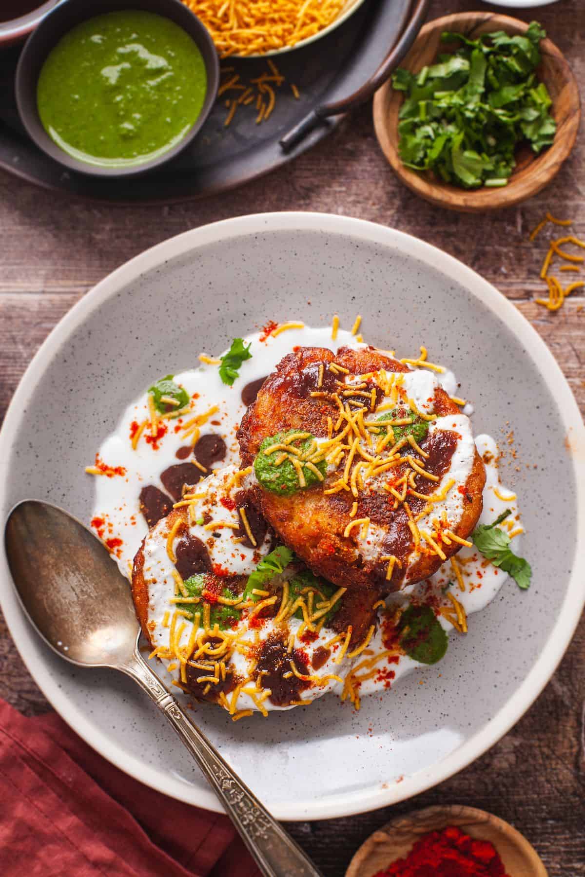 A plate of crispy aloo tikki chaat served with yogurt, sweet chutney and green chutney.