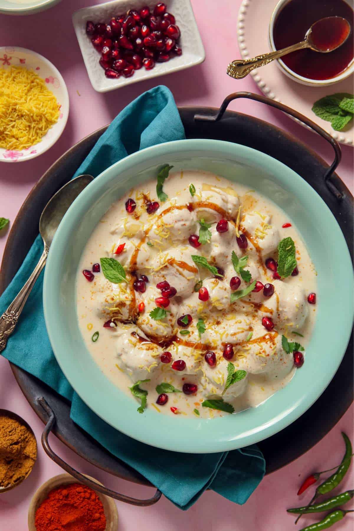 Moong Dal Dahi Vada in a blue plate topped with chaat condiments, herbs and pomegranate seeds.