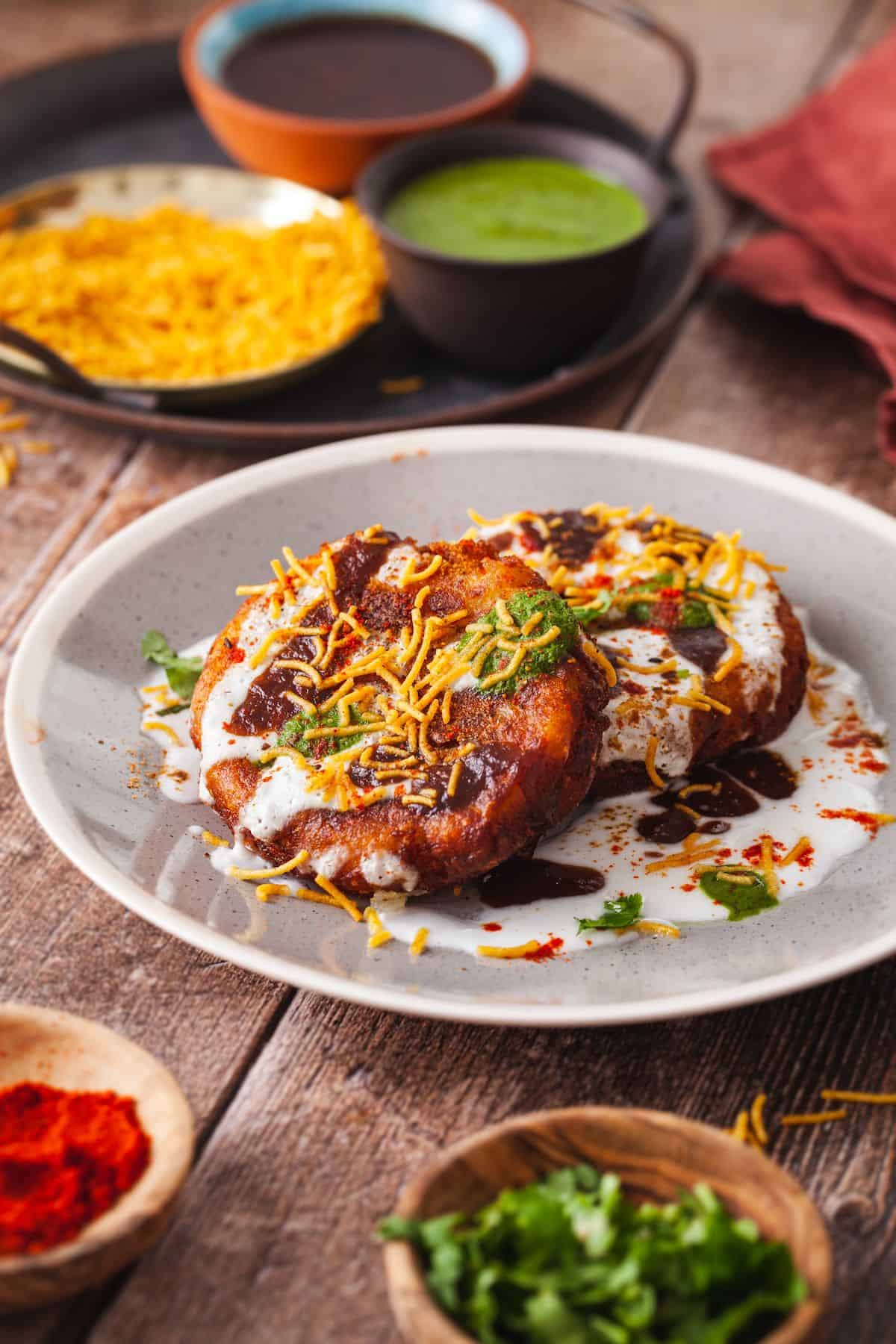 Crispy Aloo Tikki chaat served on a grey plate with chaat toppings like yogurt, chutney and chaat spices.