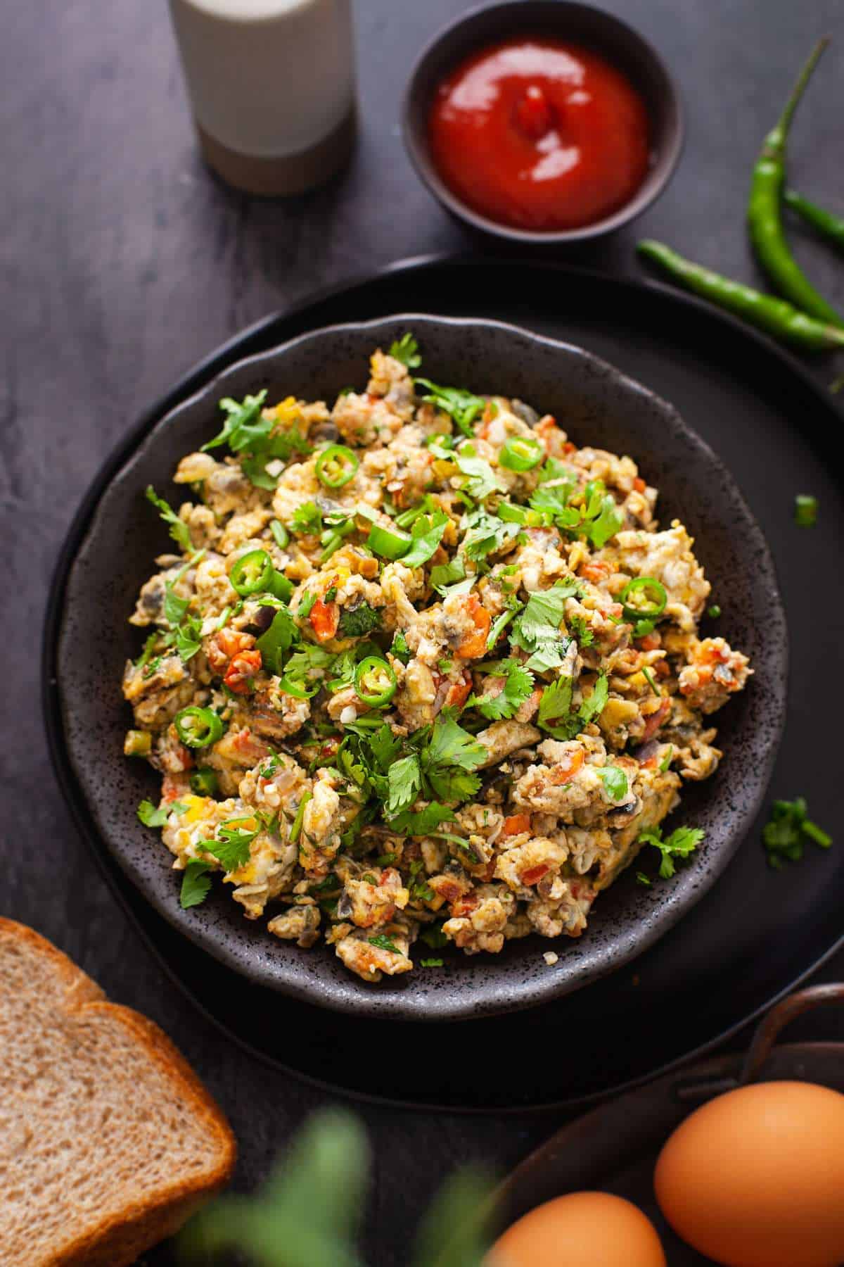 Egg Bhurji or Spiced Indian Scrambled plated in a black bowl with slices of brown bread and ketchup. 