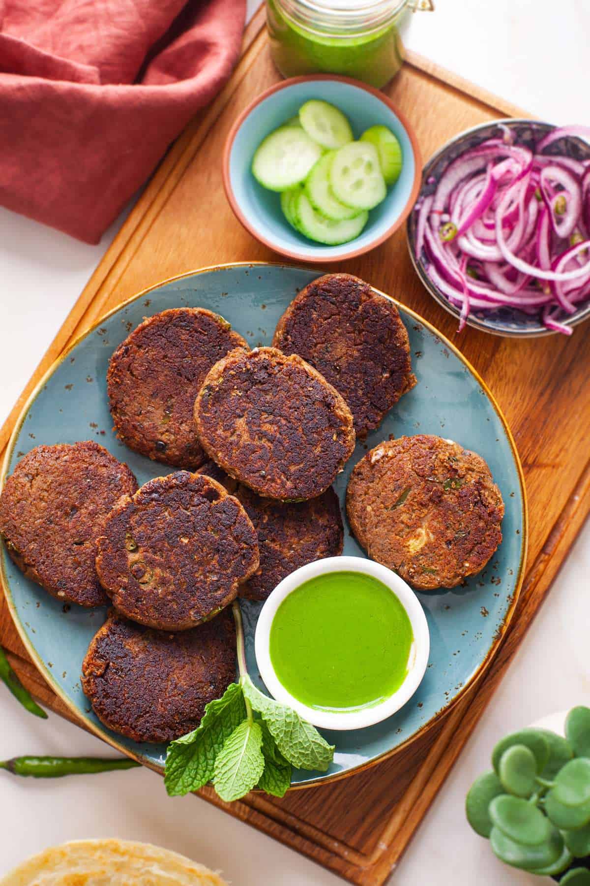 Overhead image of shami kebab on a blue platter on a wooden board served with salad and condiments.