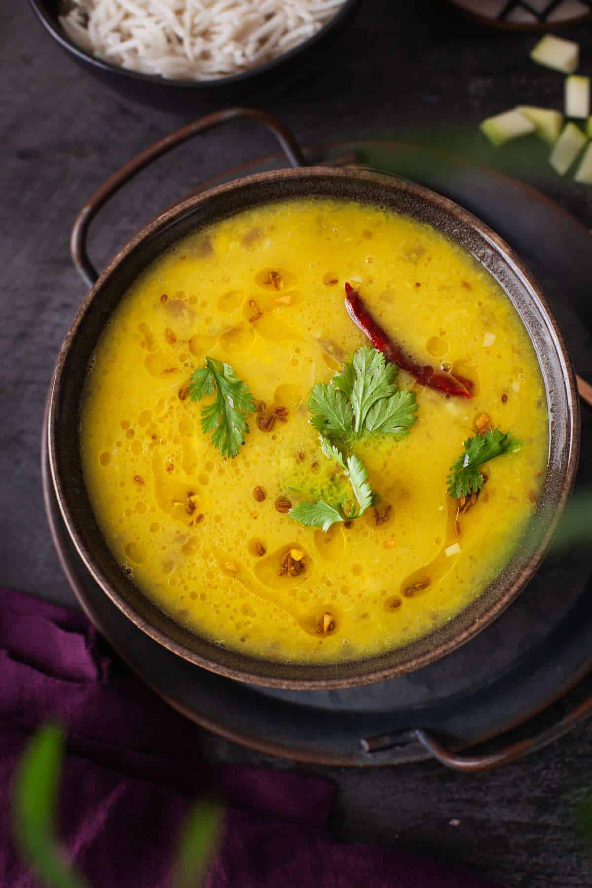 Mango Dal garnished with garlic and chili tempering & fresh cilantro is served in a black bowl with cumin rice.