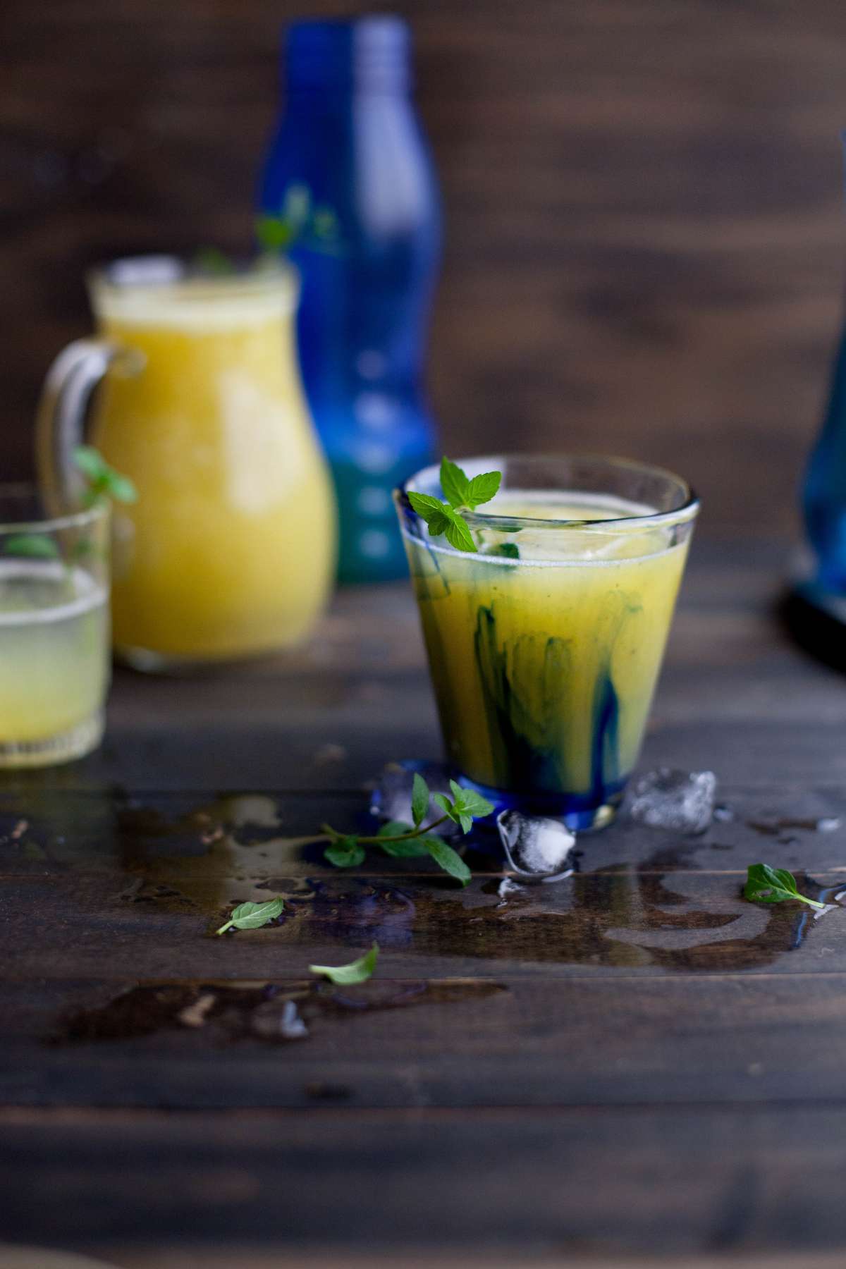 Indian green mango cooler in a cup and a large jug placed on a rustic wooden board.