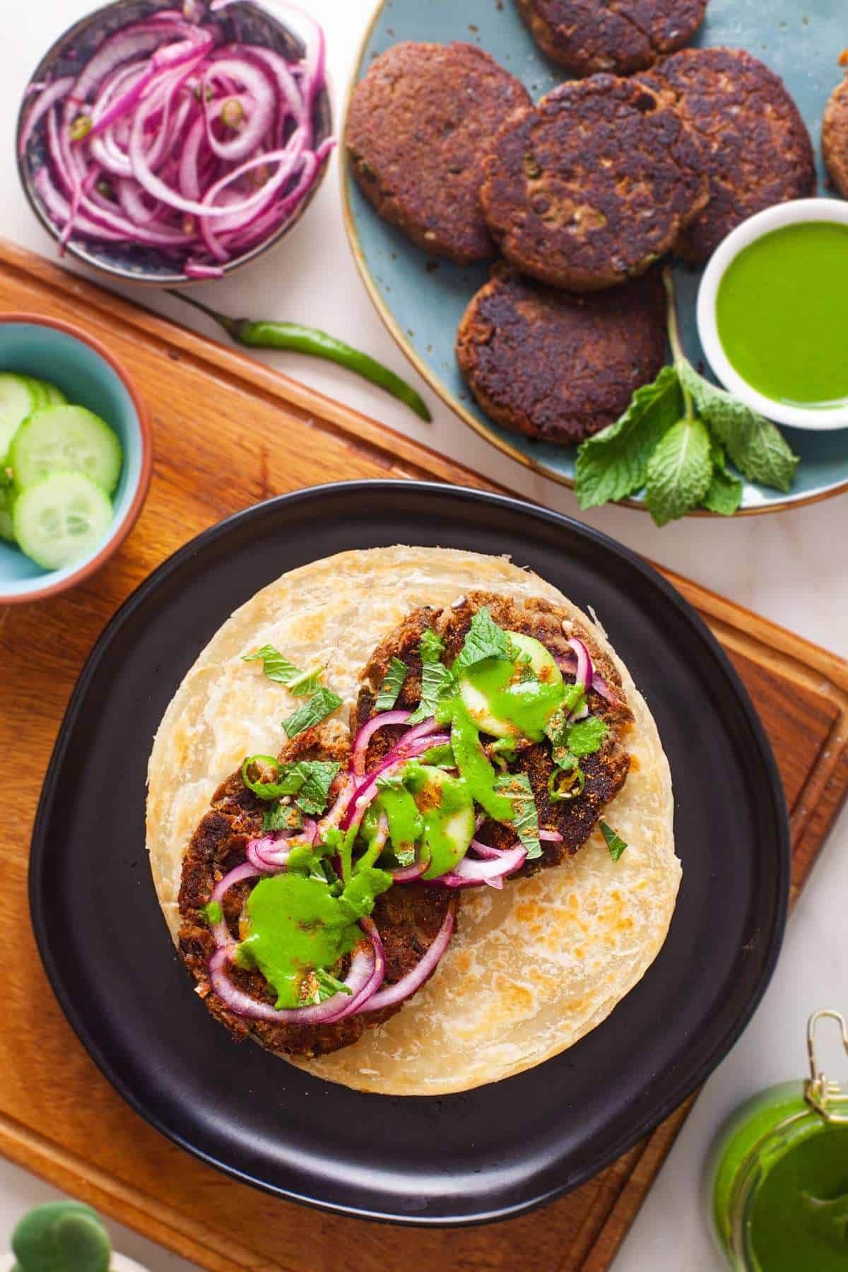 Top view picture of a shami kebab paratha roll with pickled onions and green chutney.