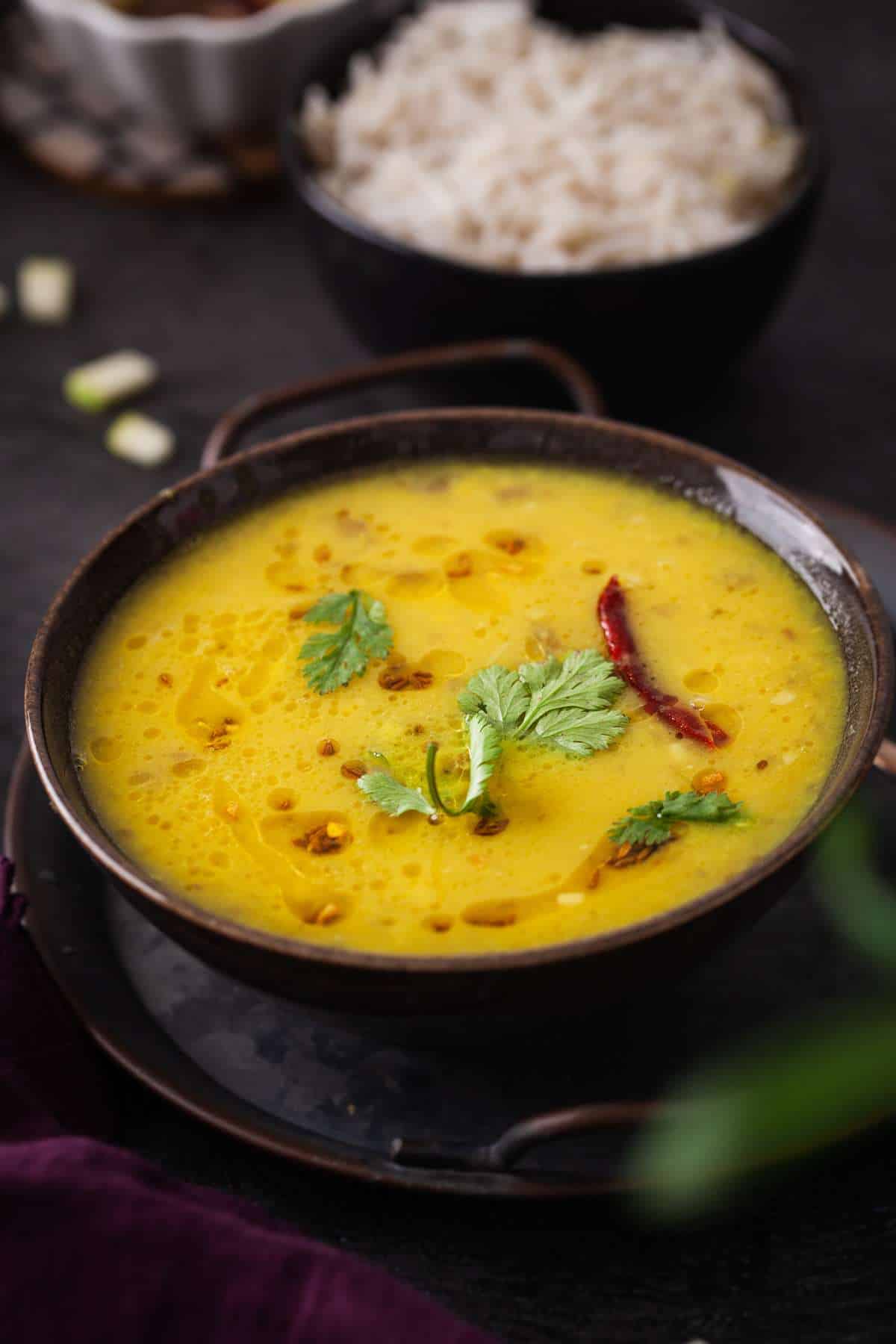 Side shot of green mango dal served in a black bowl placed over a metal tray.