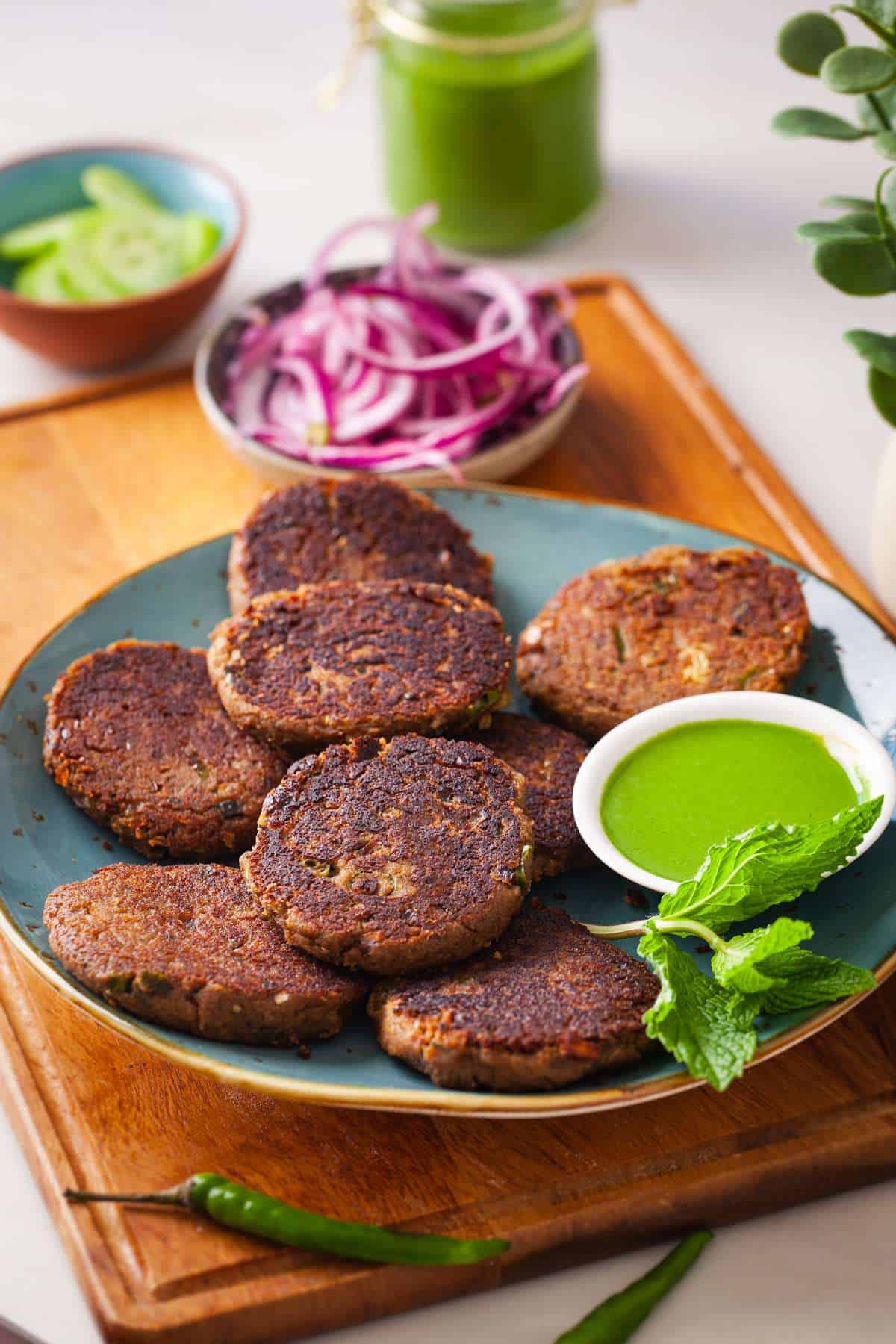 Shami Kebab on a blue plate served with green chutney, cucumber and pickled onions.