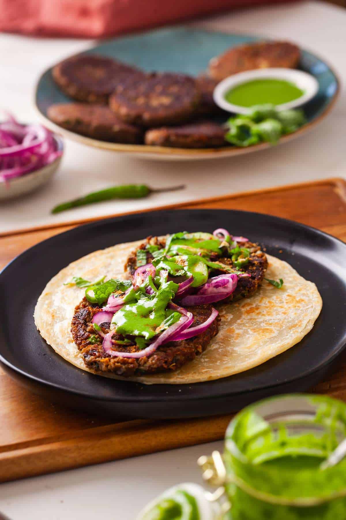 Image showing how to make a shami kebab paratha roll with pickled onions and green chutney.