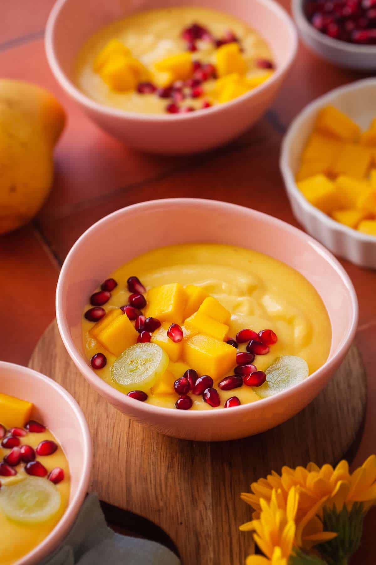 Indian Mango Custard plated in a pink bowl and topped with fresh mangoes and pomegranate seeds.