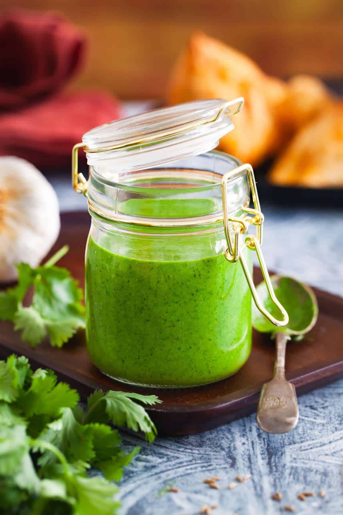 Green Chutney placed in a small glass jar with cilantro bunch and garlic around it.