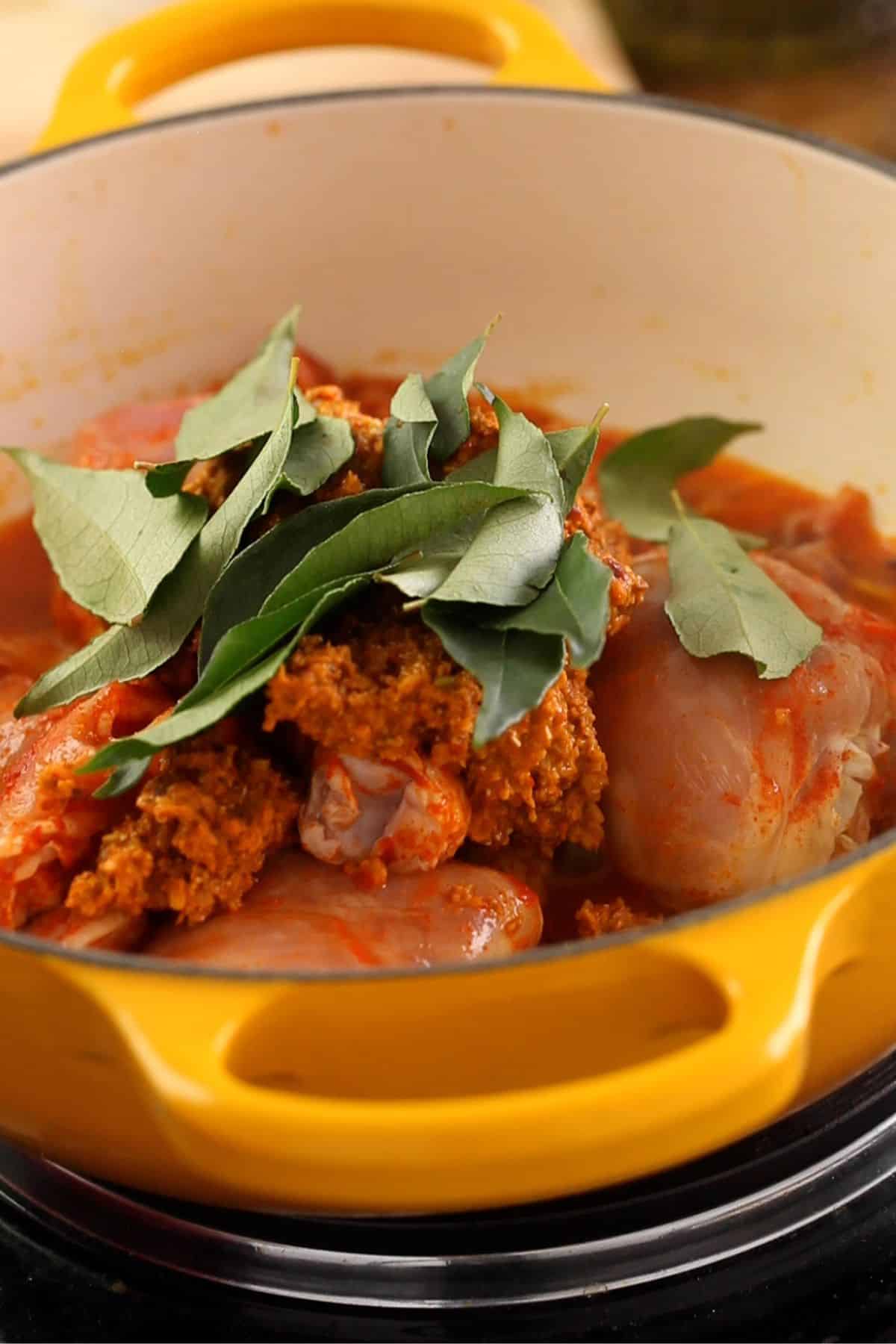 Marinated chicken, chettinad masala and curry leaves are added to the cooking pot.