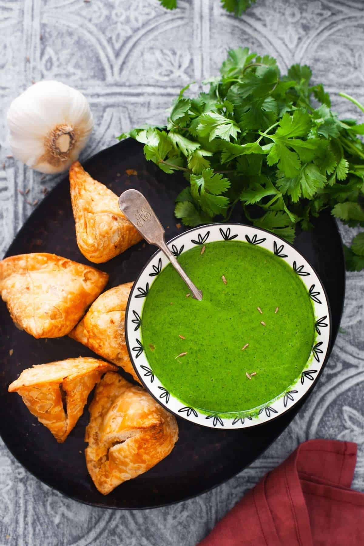A bowl of cilantro chutney with samosa placed around it. 