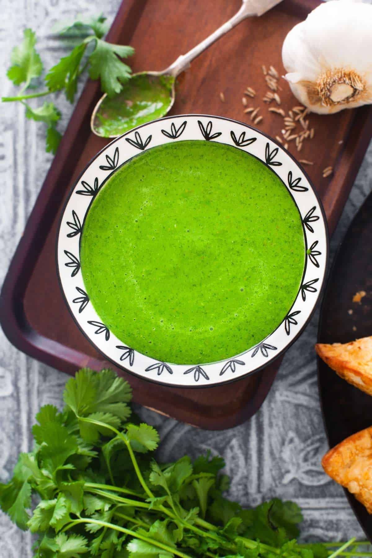 Indian Cilantro Sauce in a black and white bowl with cilantro, cumin and garlic all around it. 