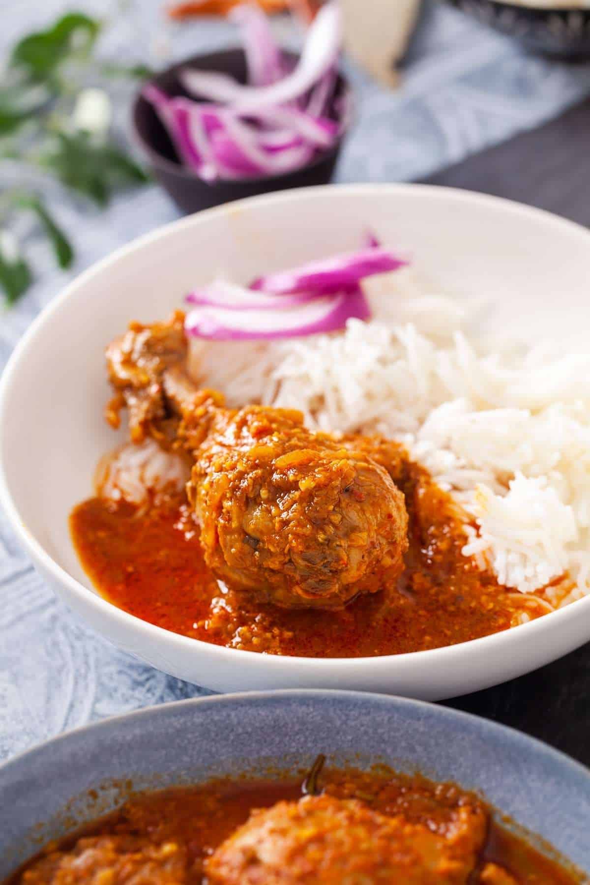 Chicken drumstick in chettinad gravy served with rice in a white dish.