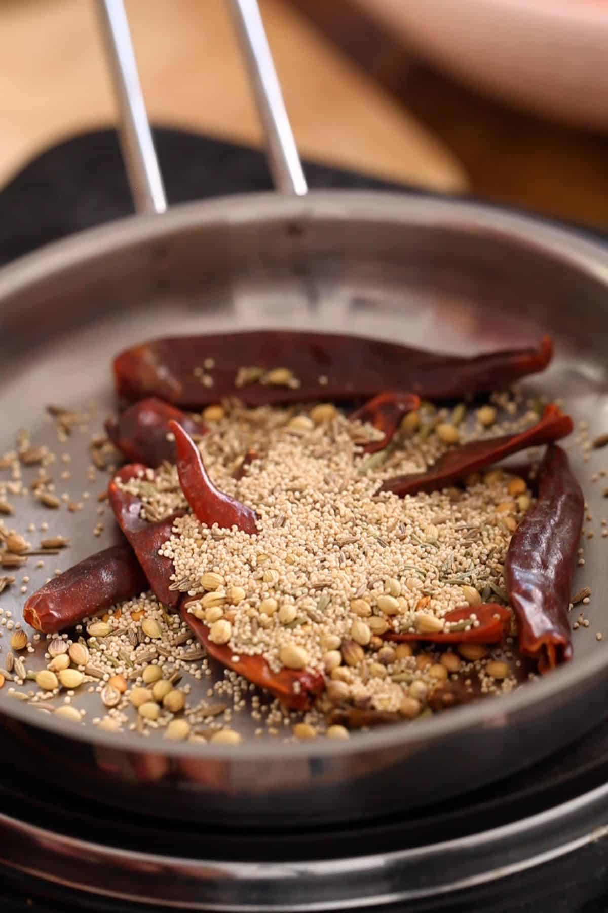 Whole spices are toasted in a stainless steel skillet.