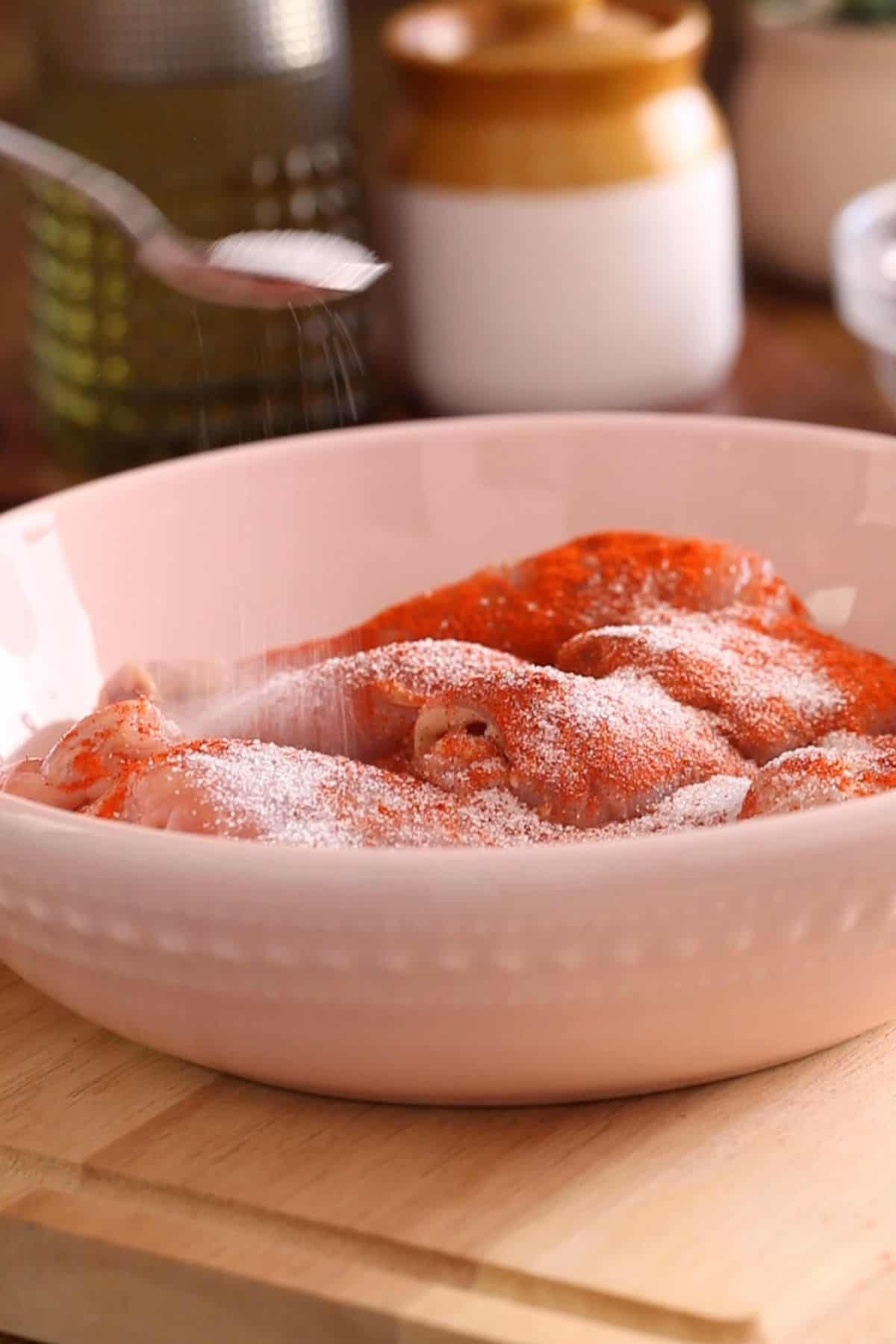 Chicken is marinated in a light pink bowl.