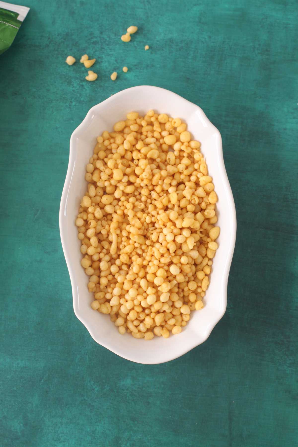 Boondi Puffs in a white dish placed on a green background. 