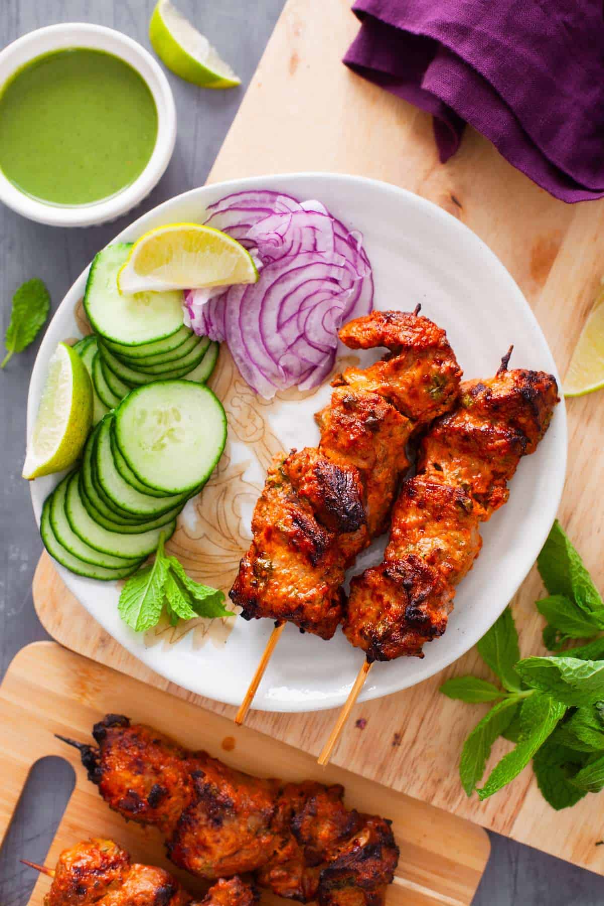 Lamb Tikka Skewers palce on a plate our sliced onions and cucumbers, lemon wedges. 