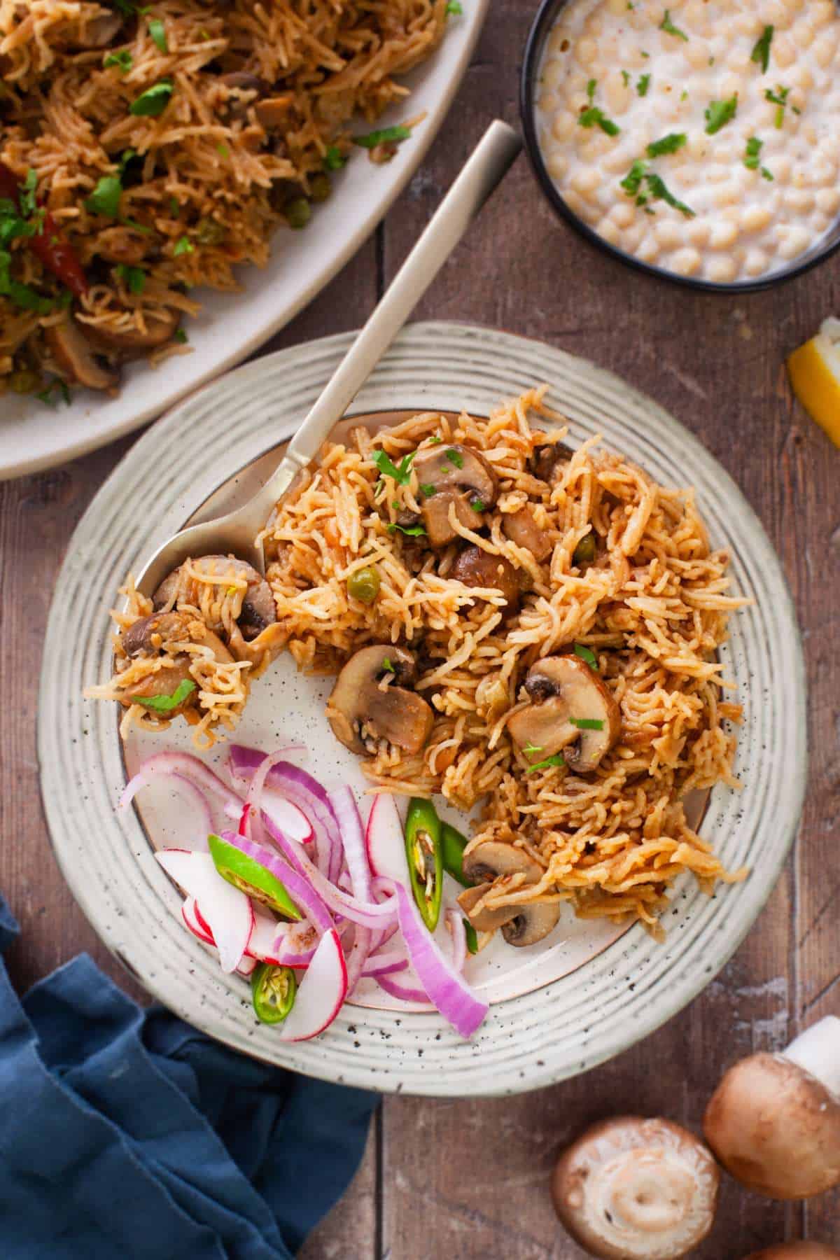 Mushroom pulao served on a beige plate with onions and chillies.