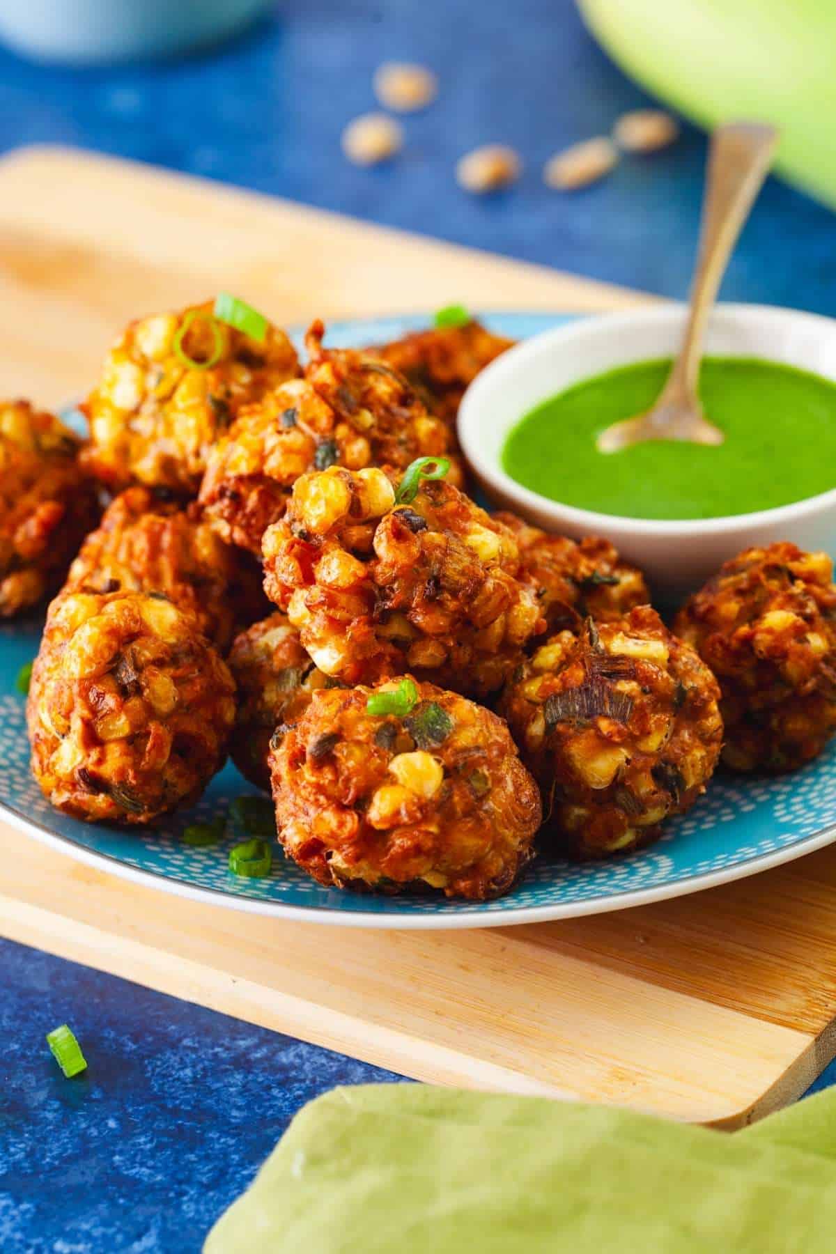 Side view of fresh corn pakoda in a plate with green chutney.