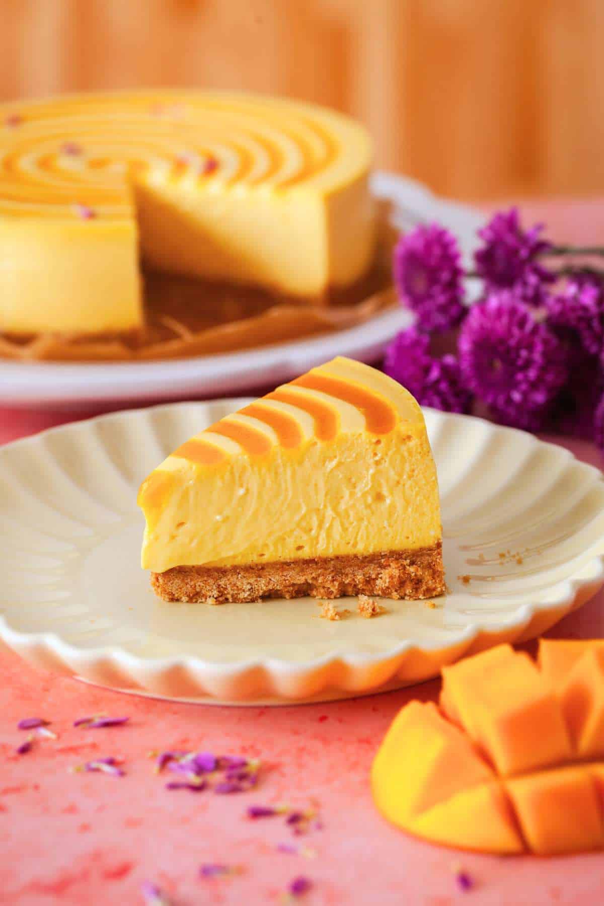 A slice of mango cheesecake placed on a beige fluted plate. 