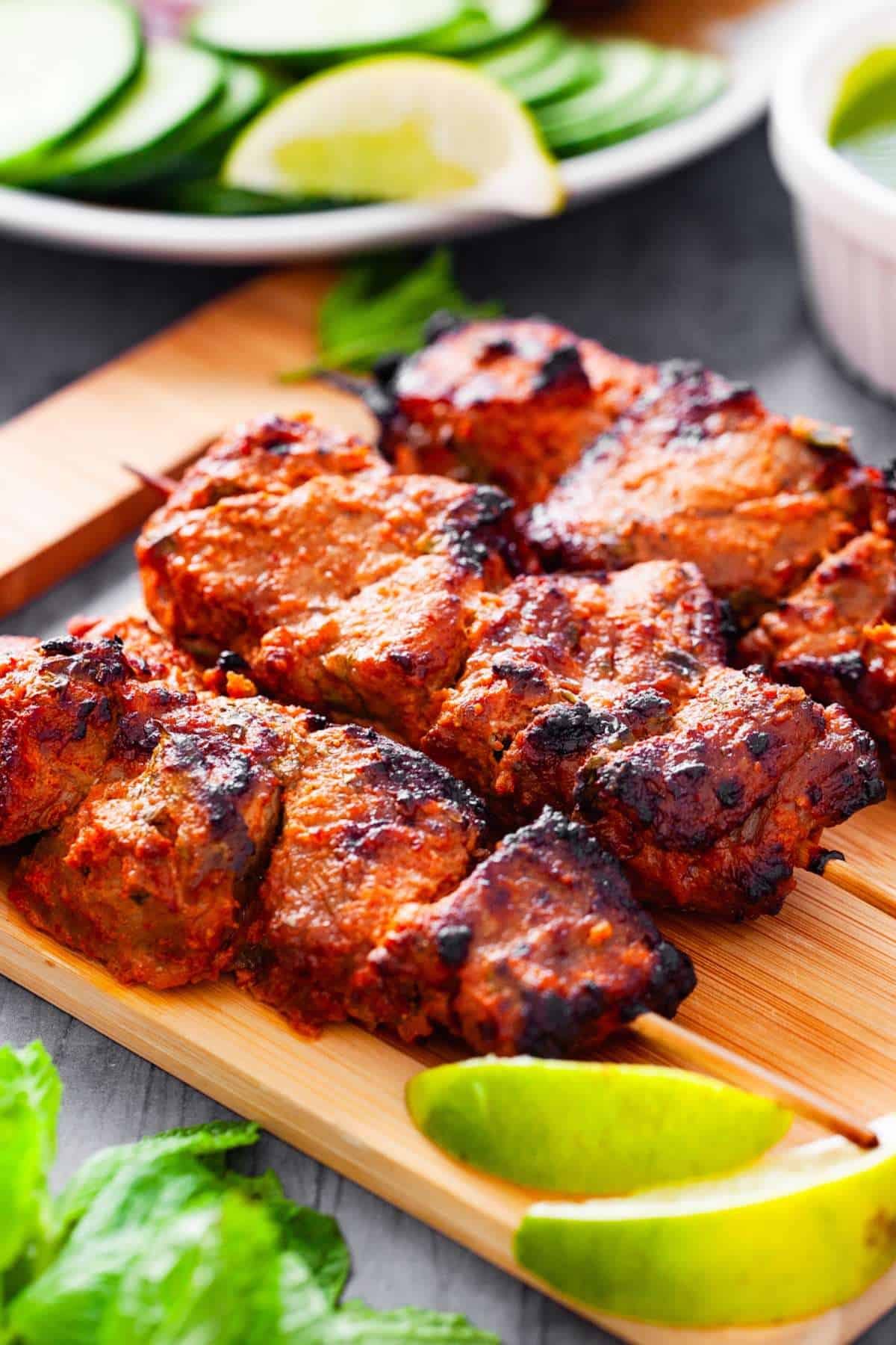 Side shot of lamb tikka on a wood board. 