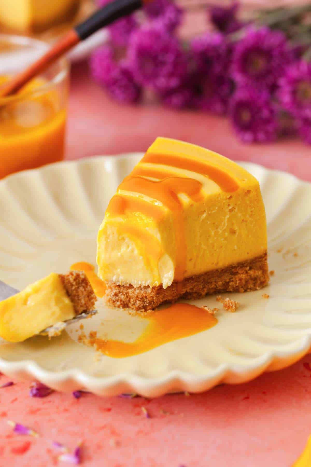 A slice of baked mango cheesecake drizzled with mango puree.