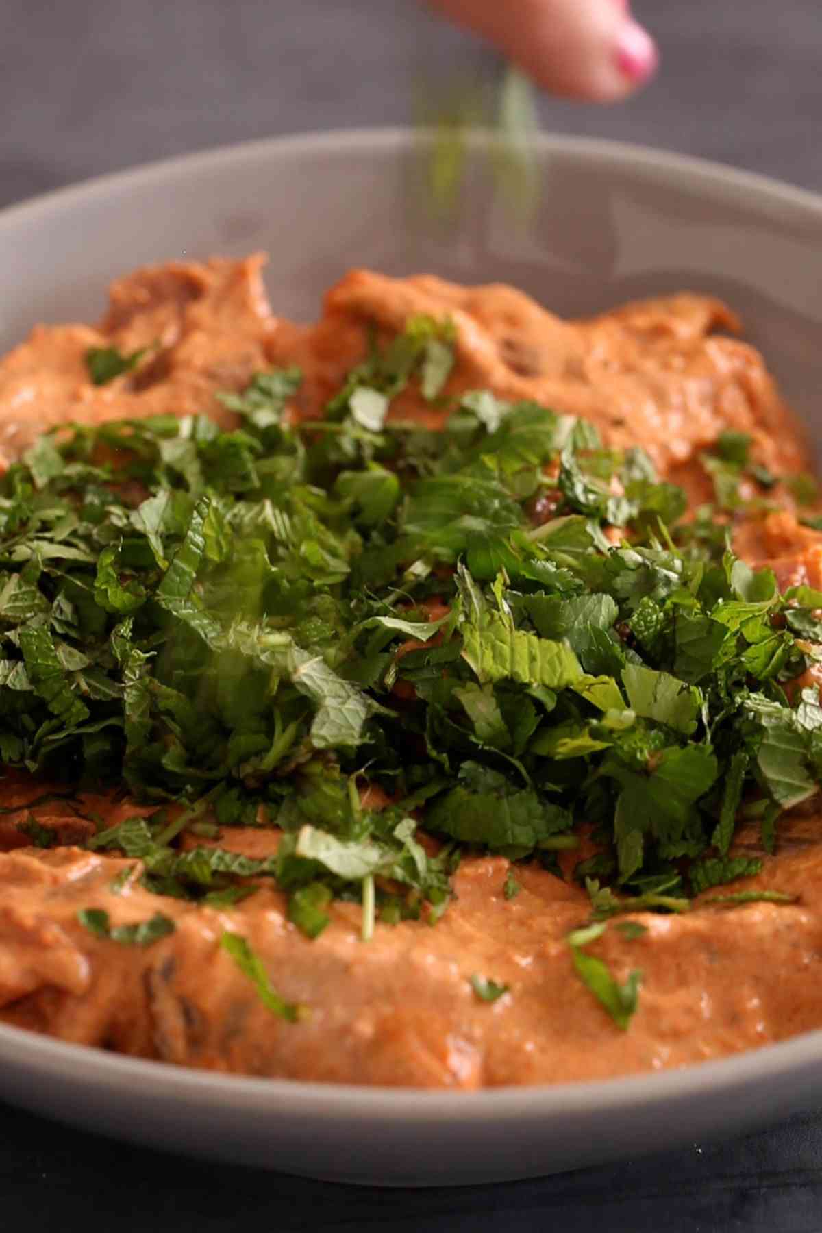 Adding fresh chopped herbs on top of marinade lamb tikka. 