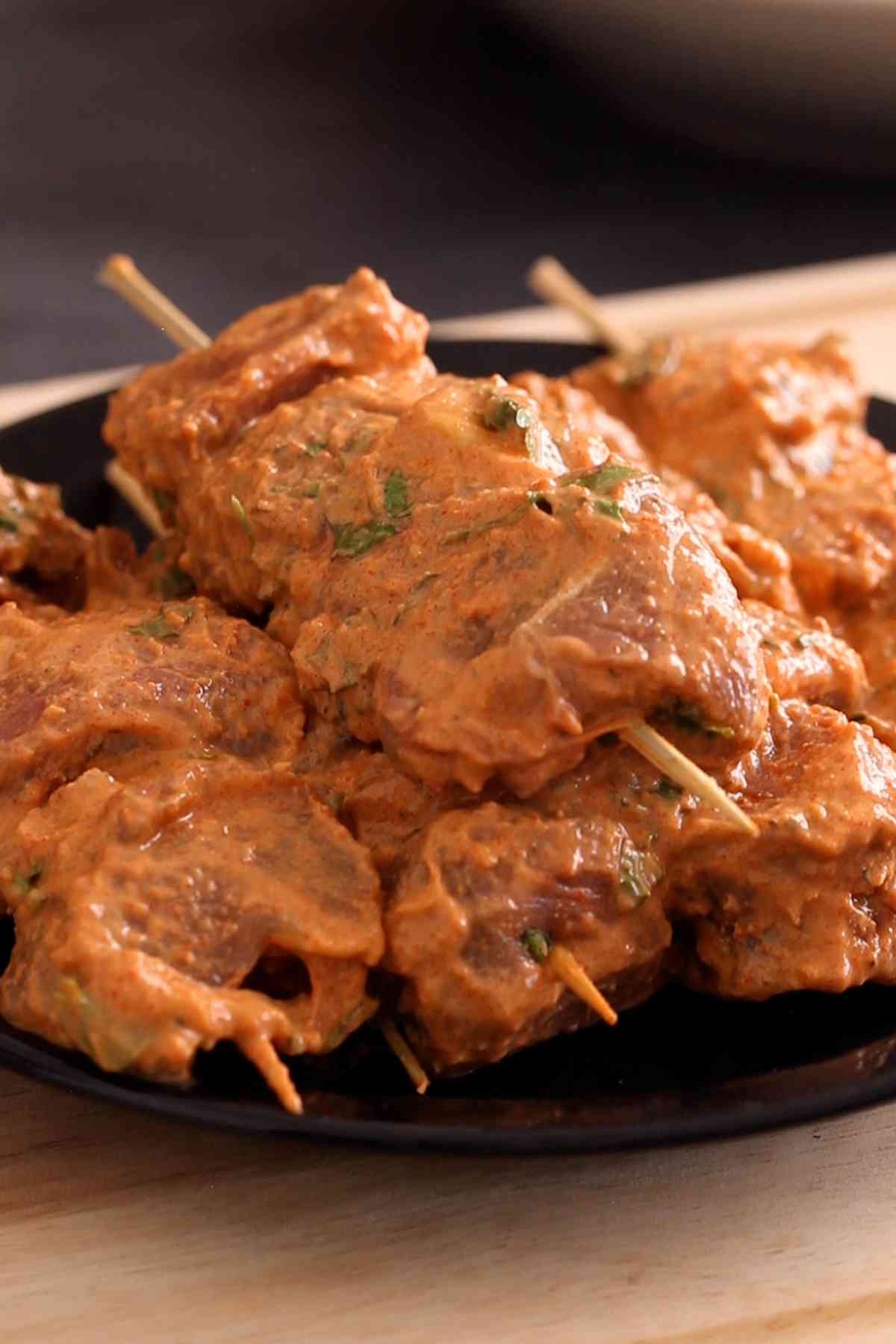 Lamb tikka skewers on a black plate. 