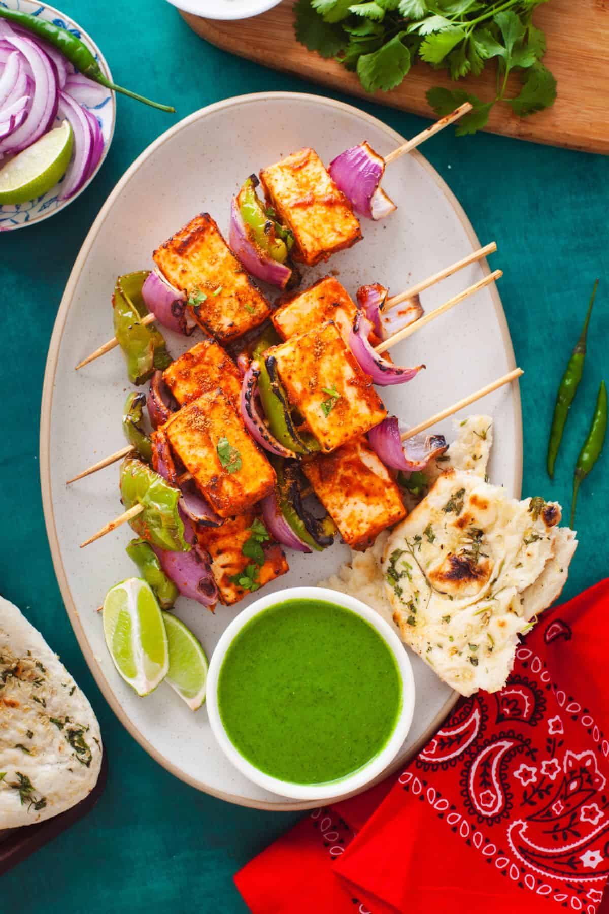Tandoori Paneer Tikka in an oval platter with green chutney and naan.