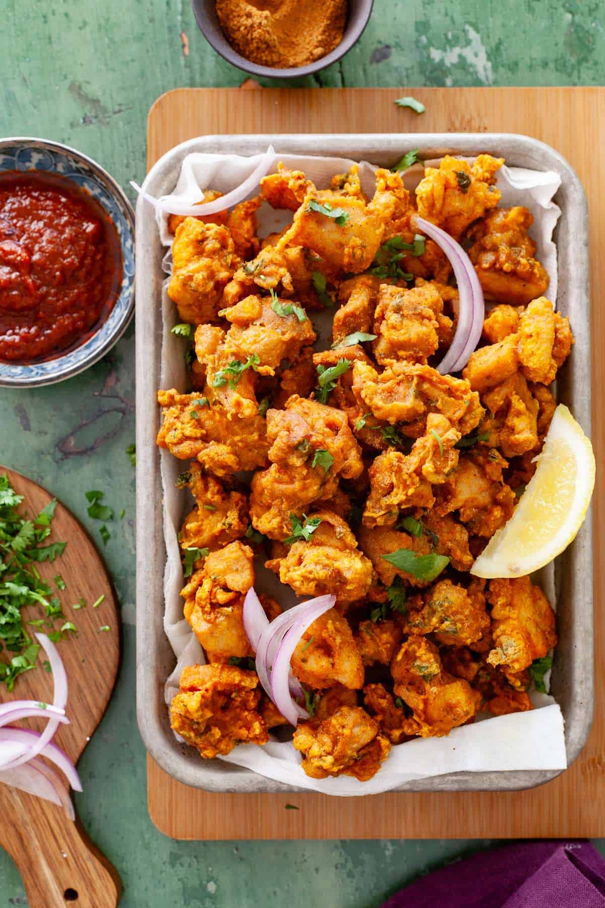 Chicken pakora in a tray served with tomato chutney & onions.