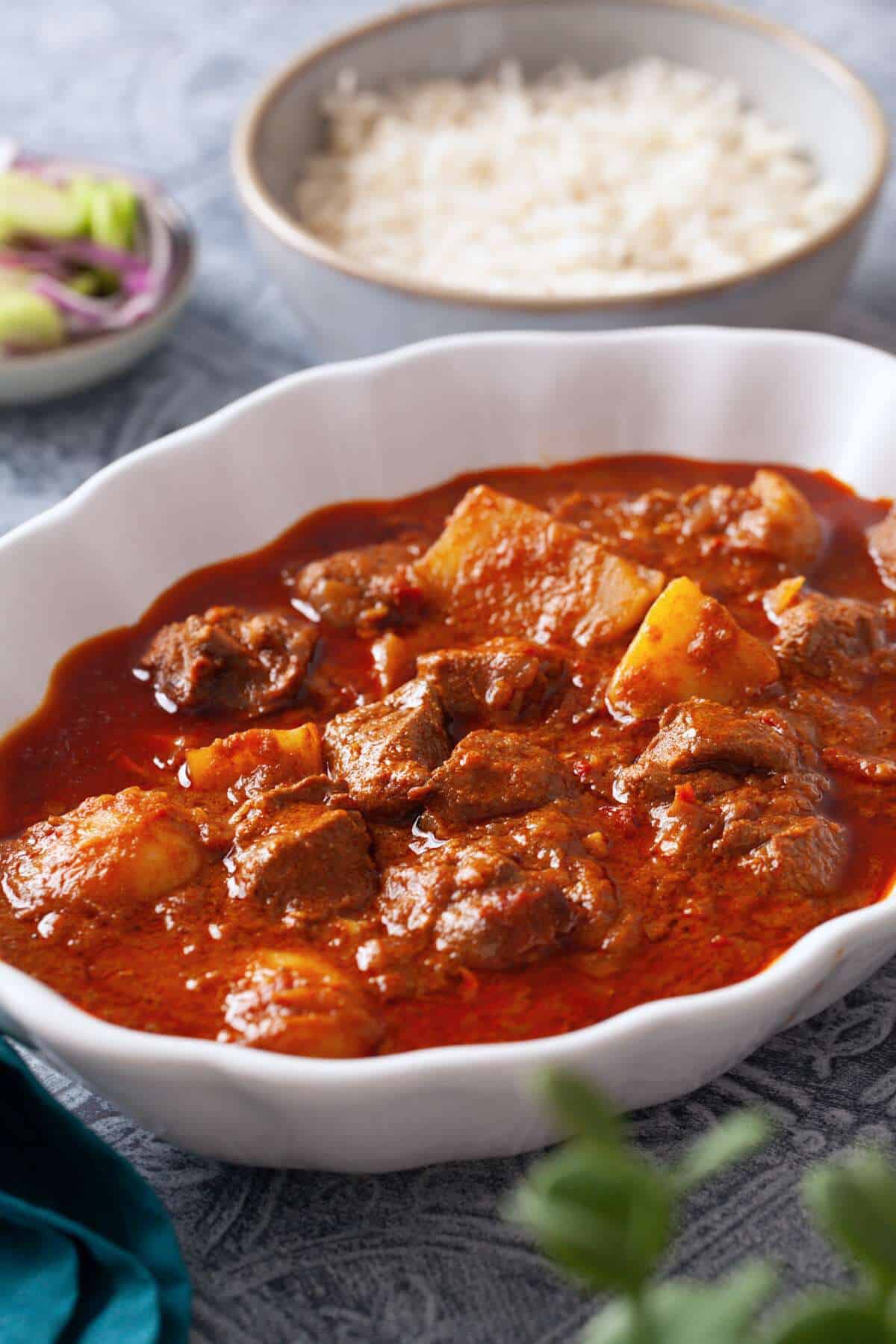Side view of indian mutton & potato curry in a white serving bowl.