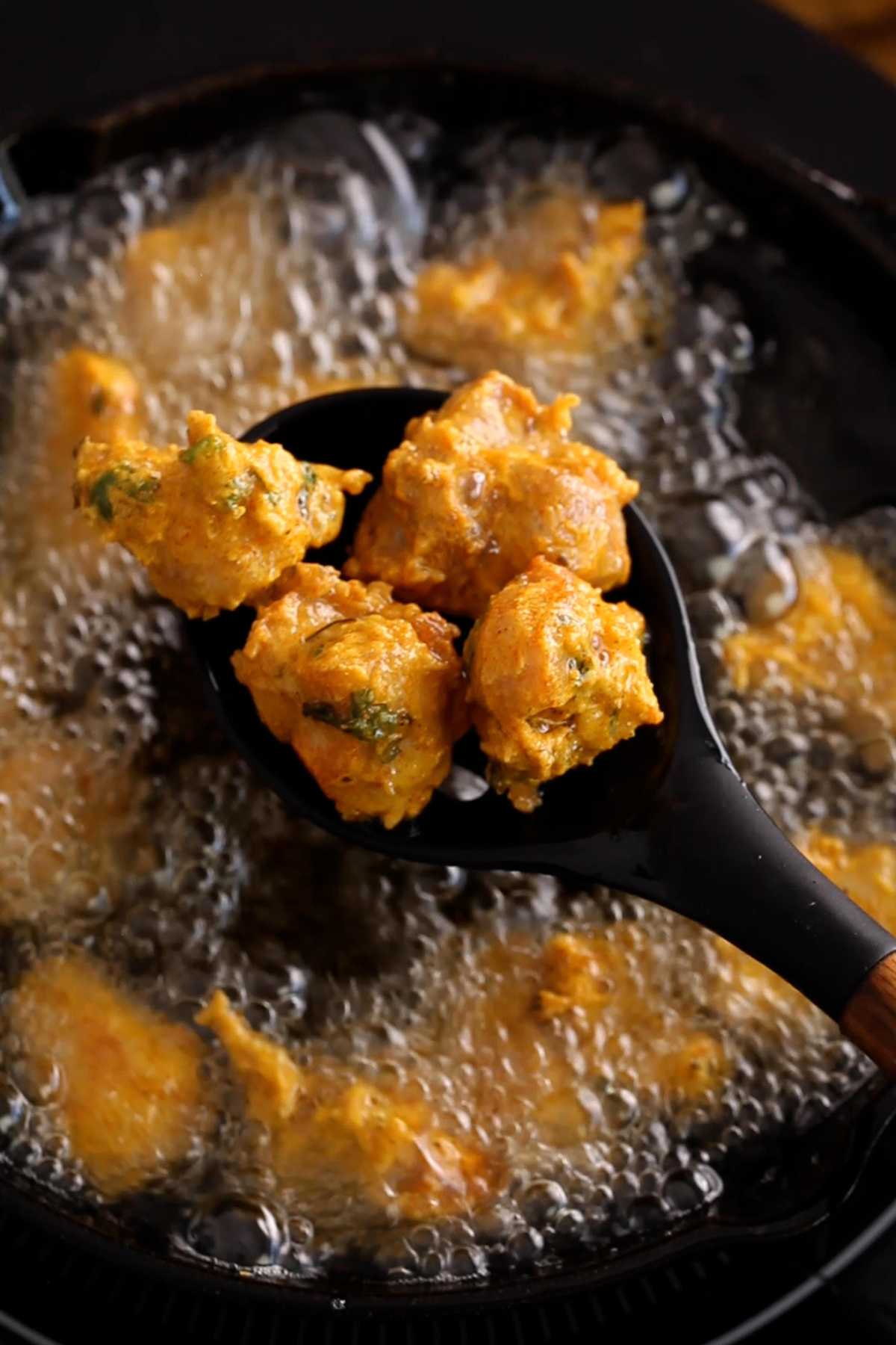 Crispy chicken pakora in a black spoon.