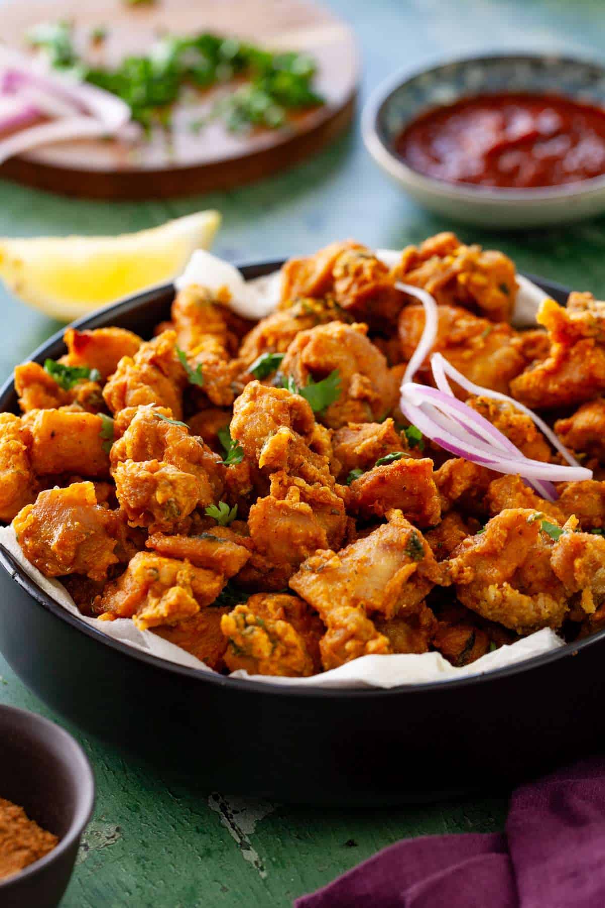 Side shot of indian chicken fritters served in a black bowl. 