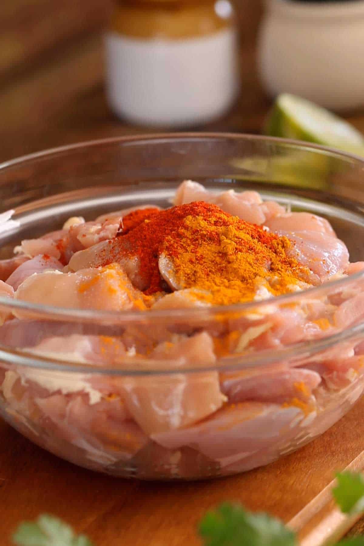 Chicken mixed with spice powders in a glass bowl. 