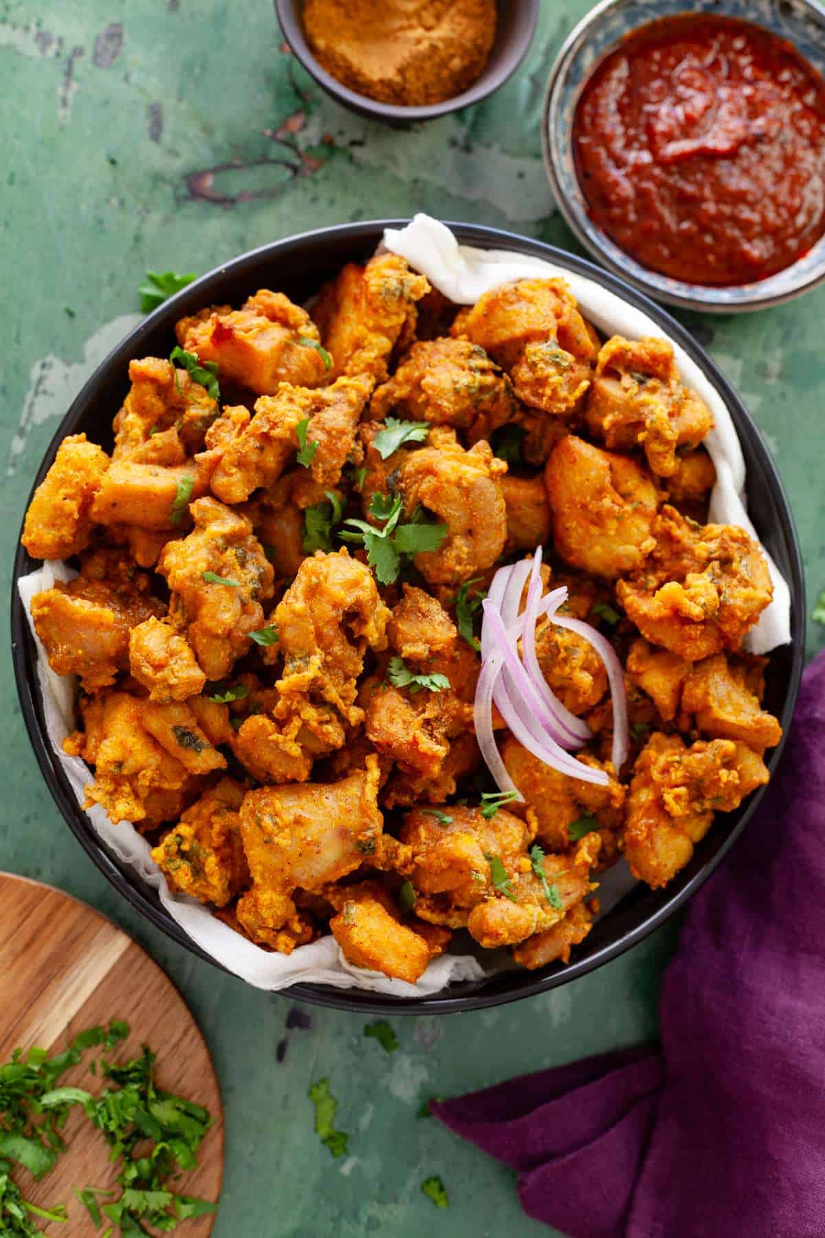 Chicken pakora with sliced onions in a large black dish.